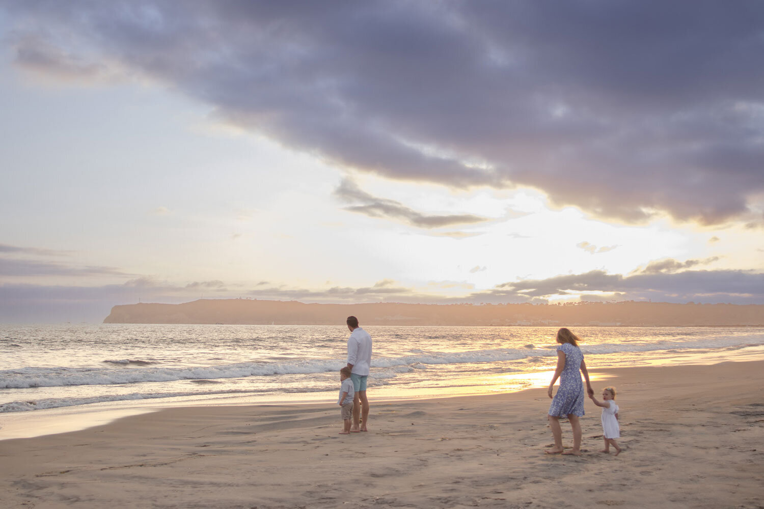 A family of four walking along the beach during sunset, enjoying a peaceful stroll by the ocean