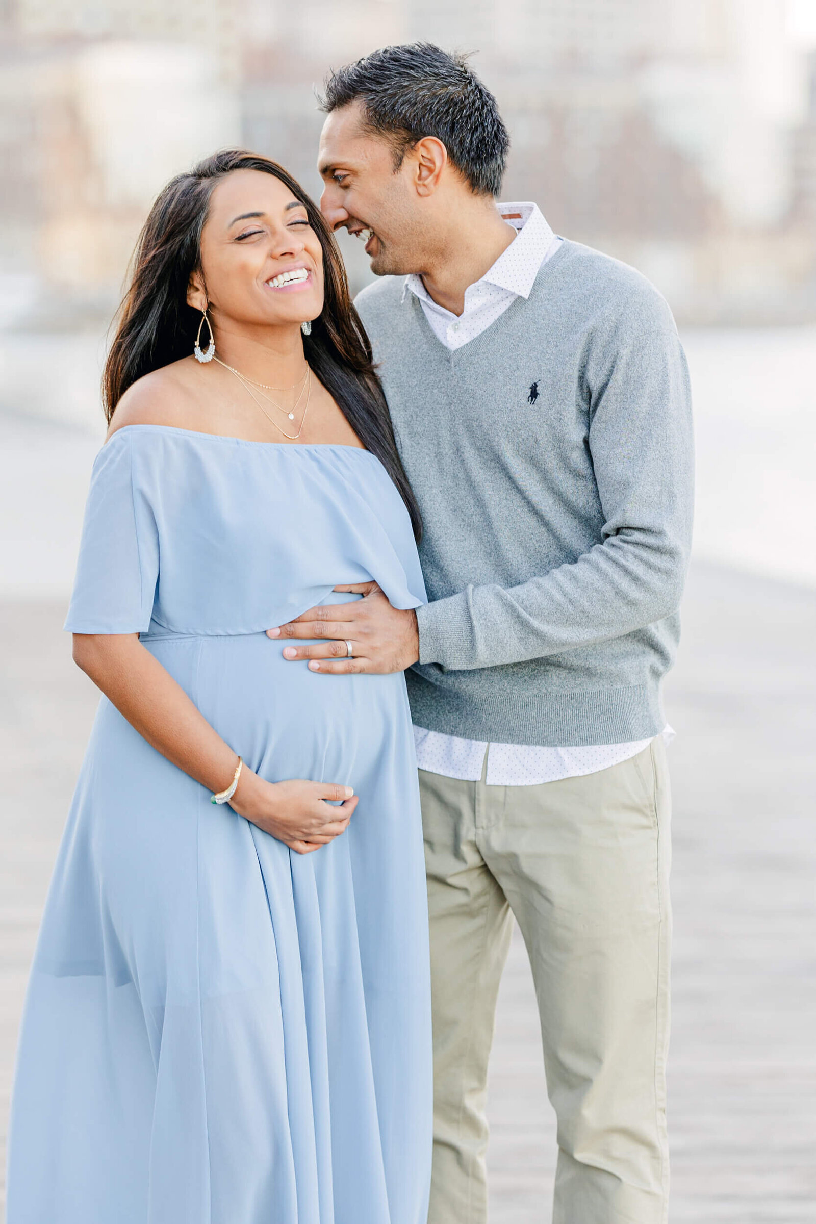 Man whispers something into his pregnant wife's ear as she laughs