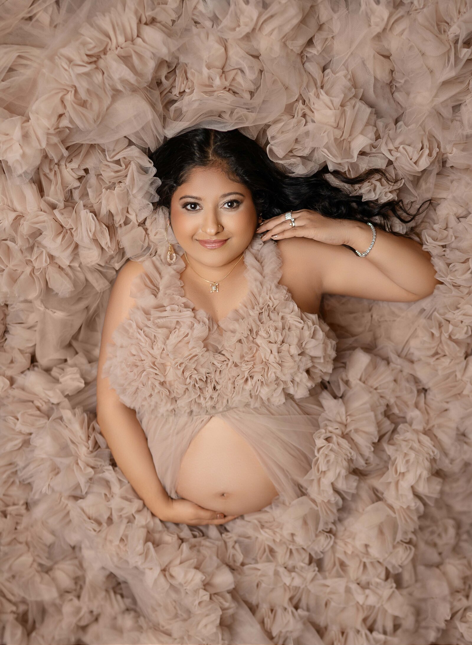 Pregnant women laying in a large pile of ruffled tulle and holding baby bump. Photo taken by Jenni Nikki at Maternity photo studio in Atlanta, GA.