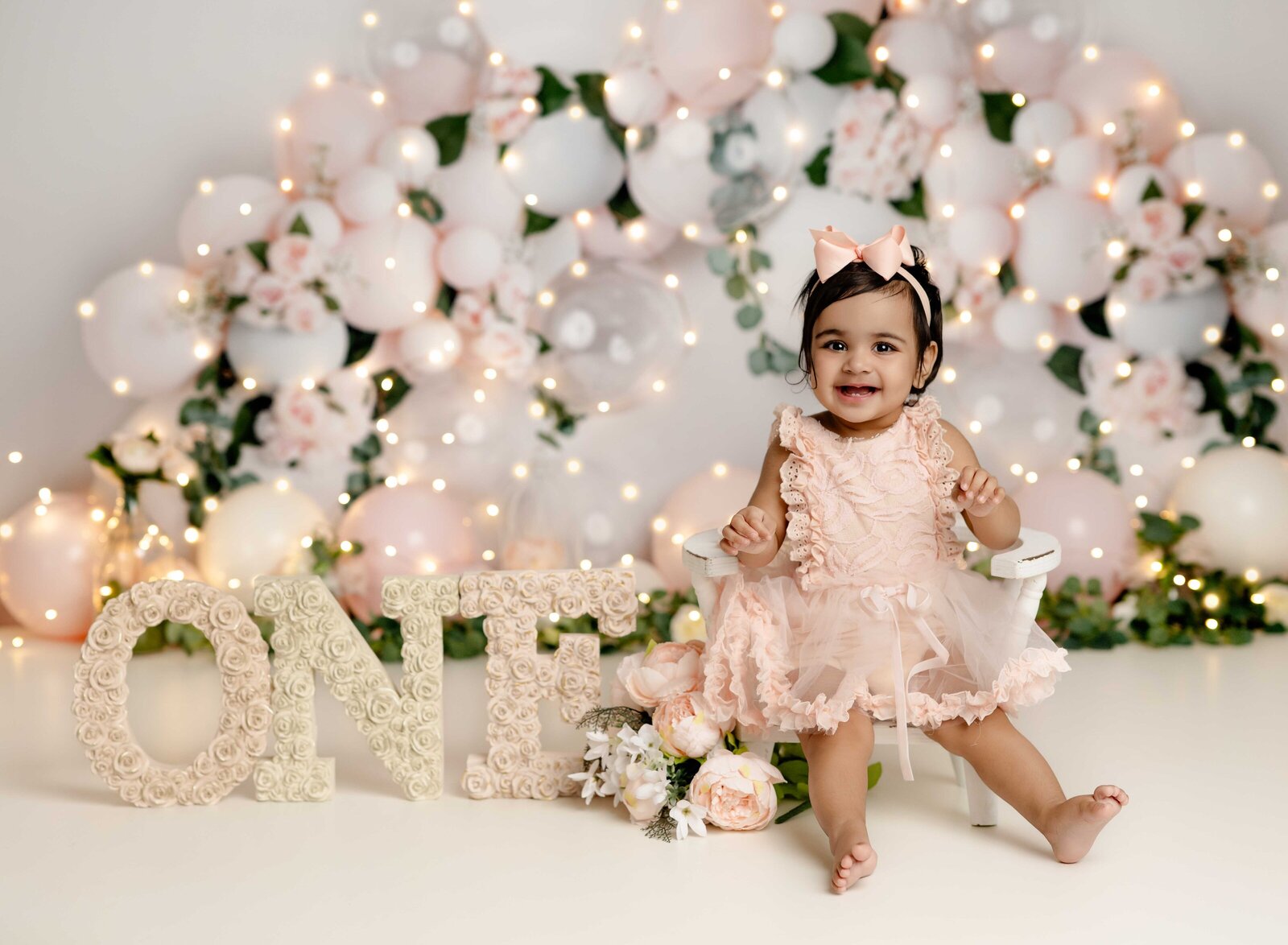Baby in peach dress sitting next to ONE letters. Cake Smash photo taken by Jenni Nikki in Atlanta, GA