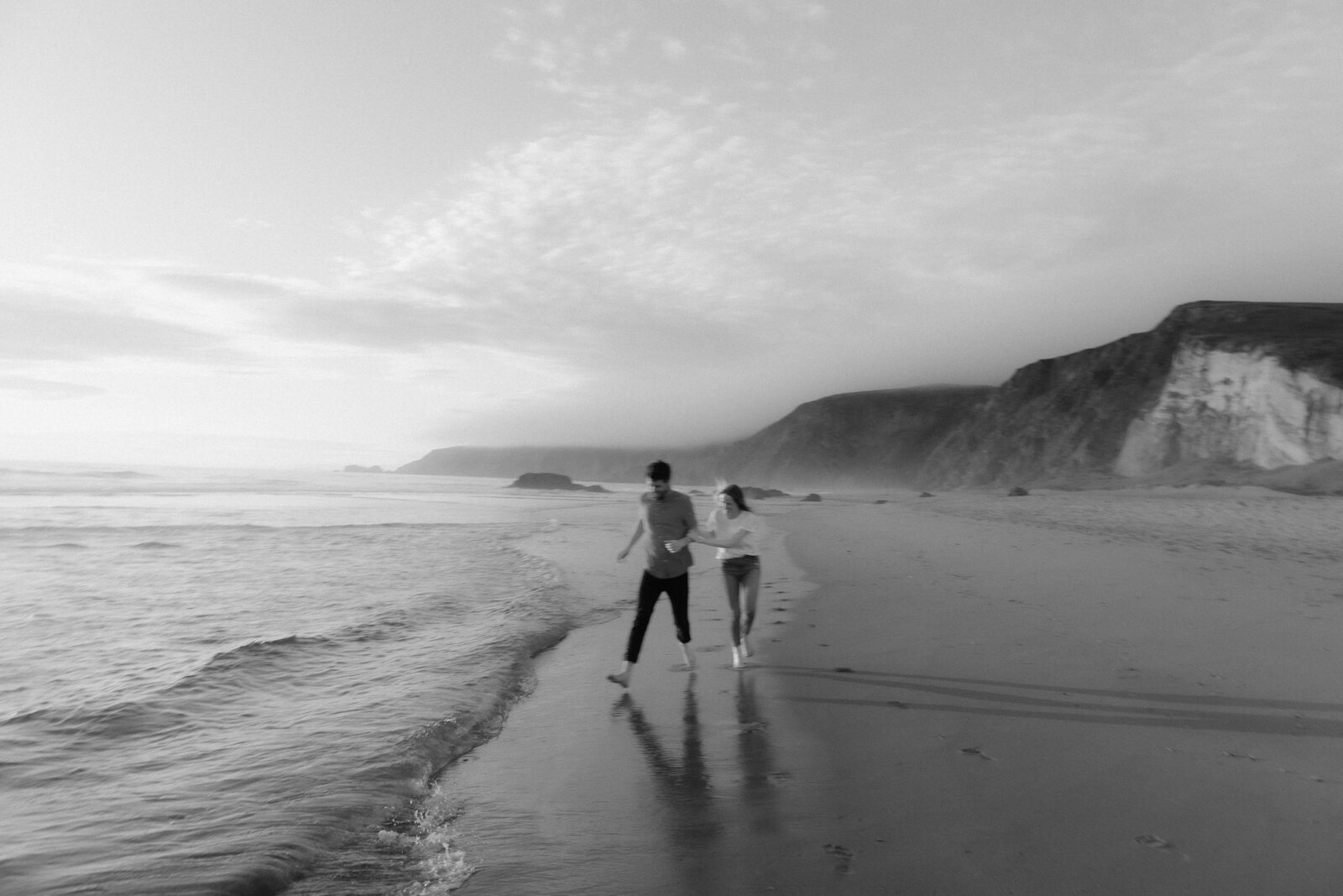 A couple runs along the shoreline, their laughter and movement captured in an editorial wedding photography style.
