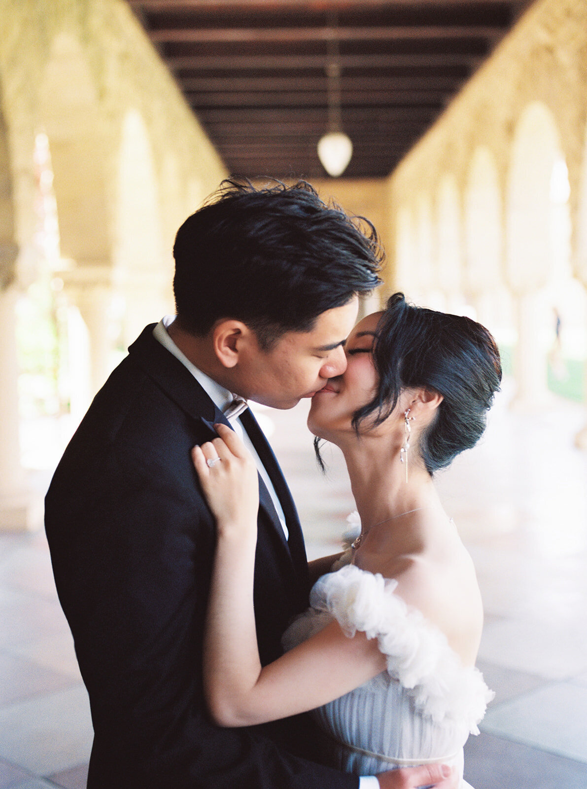 The bride and groom share a romantic kiss under the arches of the stunning Stanford Memorial Church, creating a timeless wedding memory.