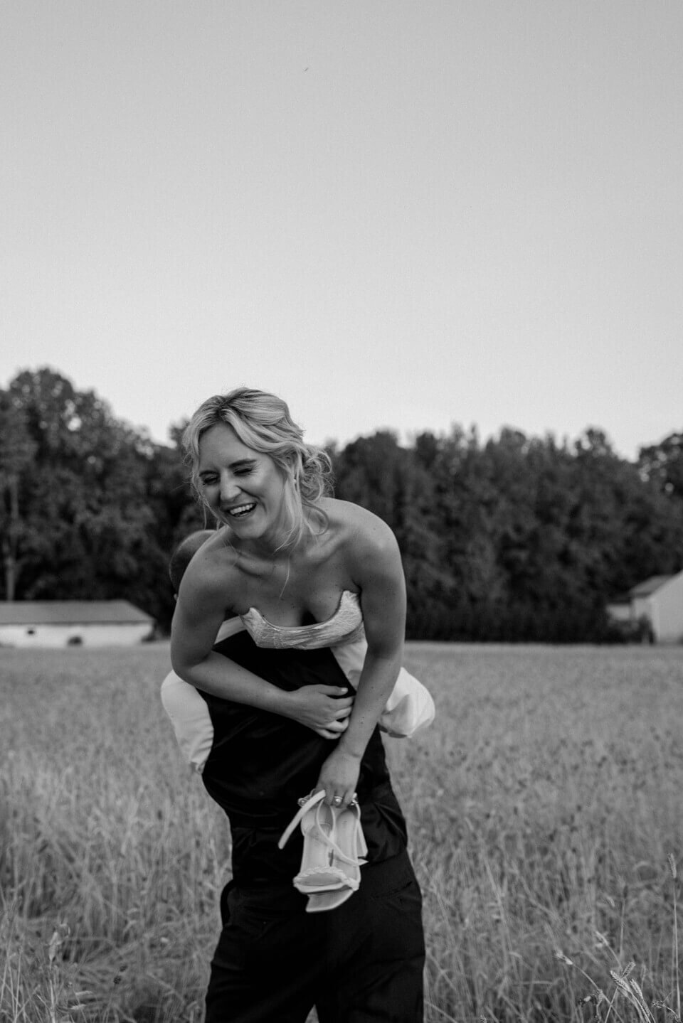 bride over grooms shoulder in field spinning and laughing while holding shoes photo