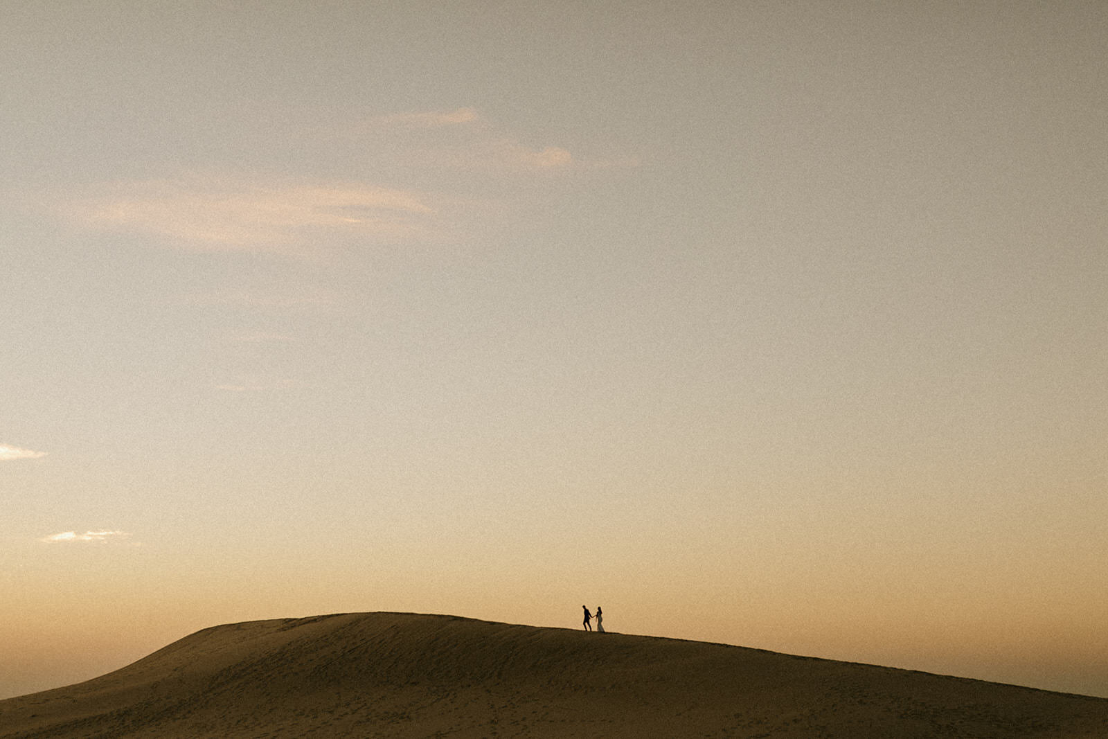 A wedding couple walking along a sand dune in the distance captured by a West Michigan photographer.