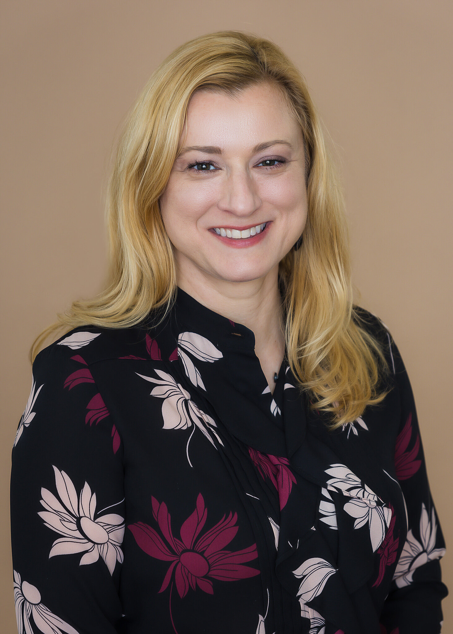 woman with blonde hair and black flower shirt smiling at camera