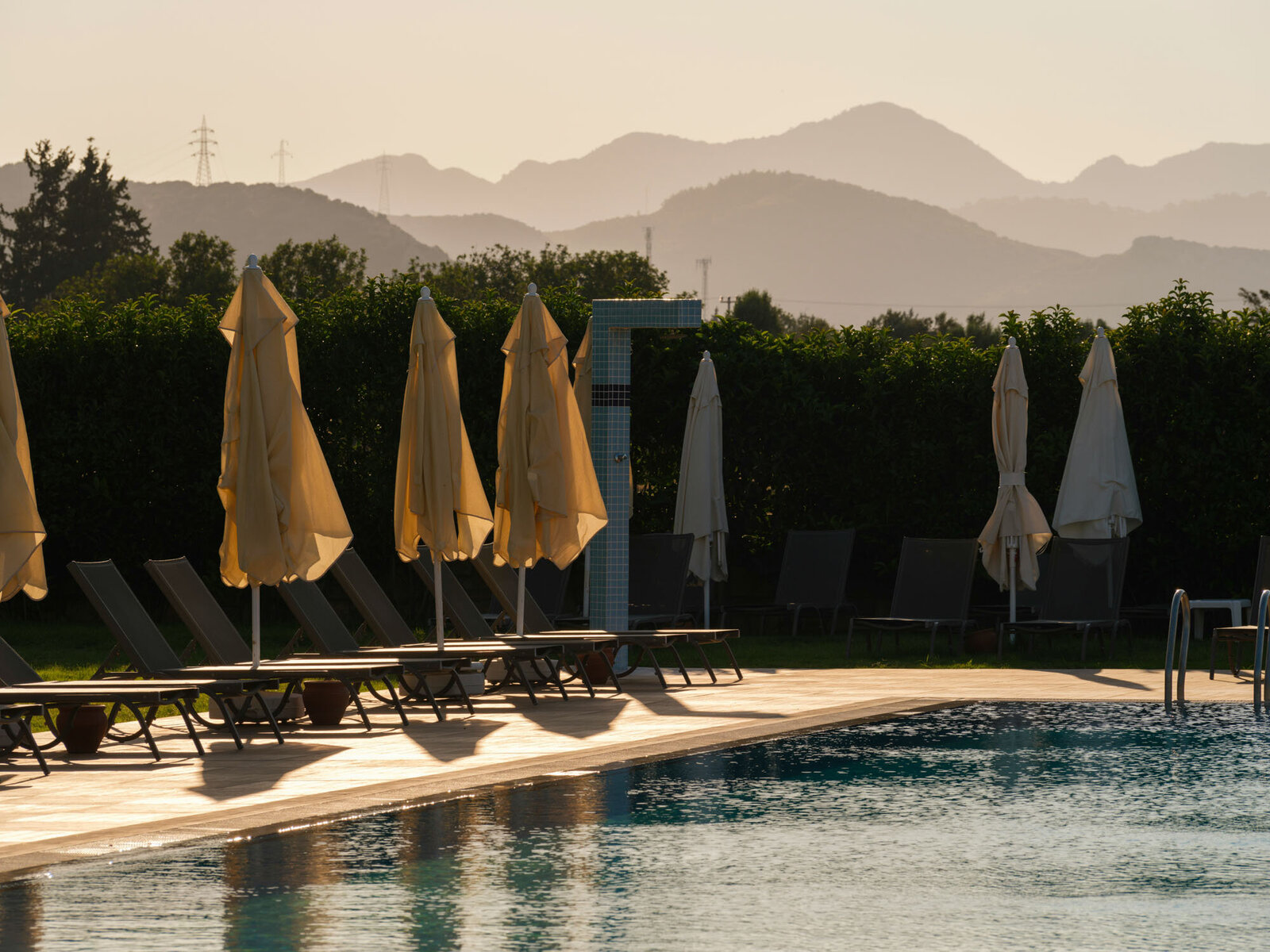 A swimming pool with chairs and umbrellas and mountains in the background