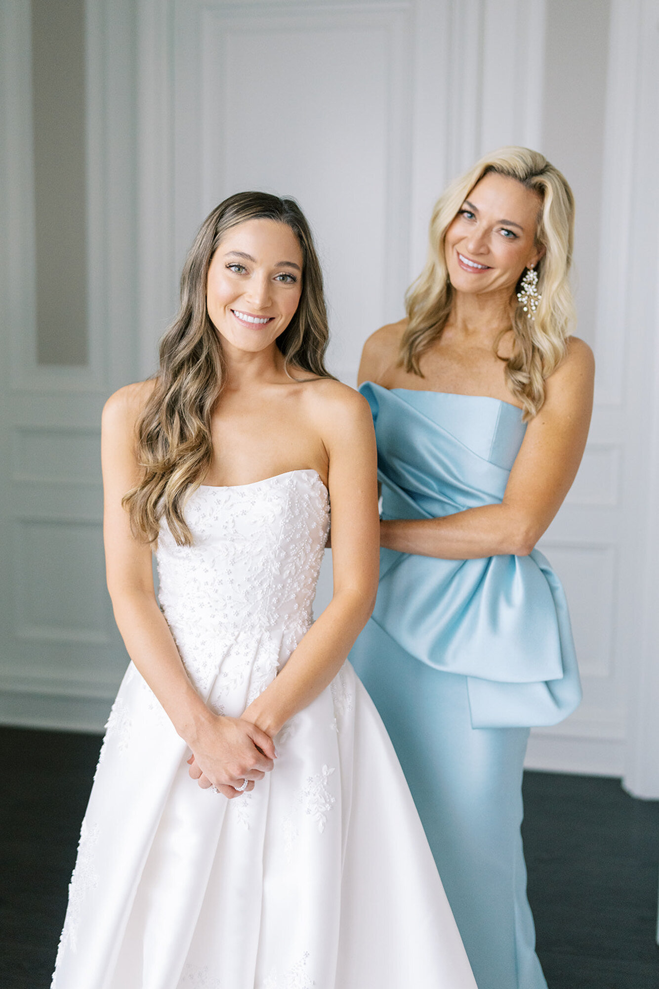 mother of the Bride wearing blue dress helping bride put dress on
