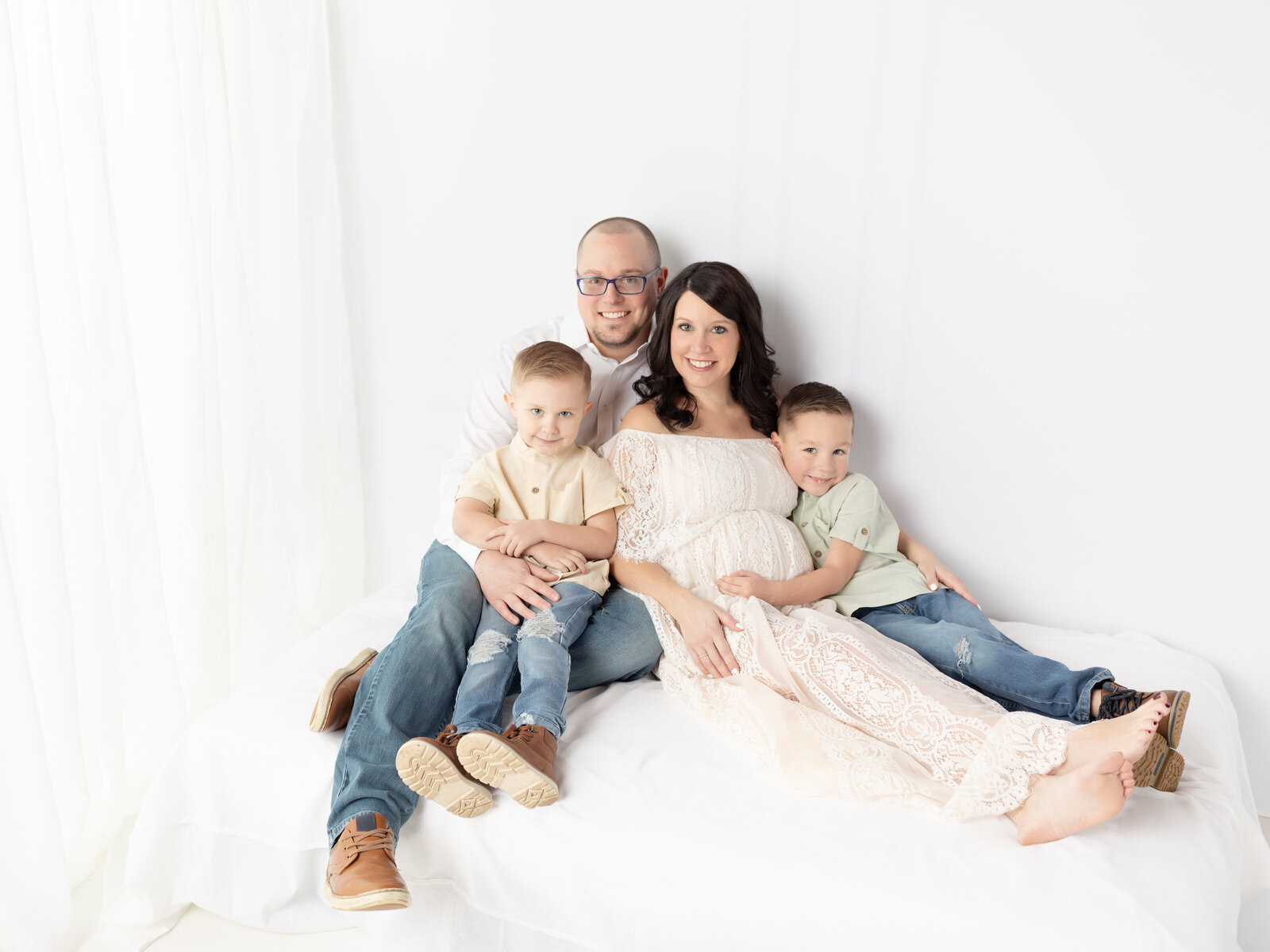 family sitting on white bed for maternity portraits Cleveland maternity photographer