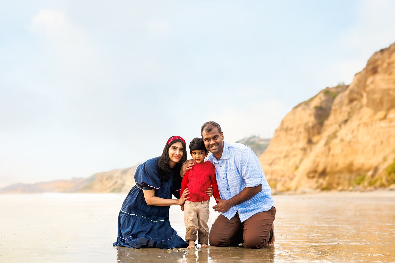 Family of three posing for a beach portrait at Scripps Pier in La Jolla California