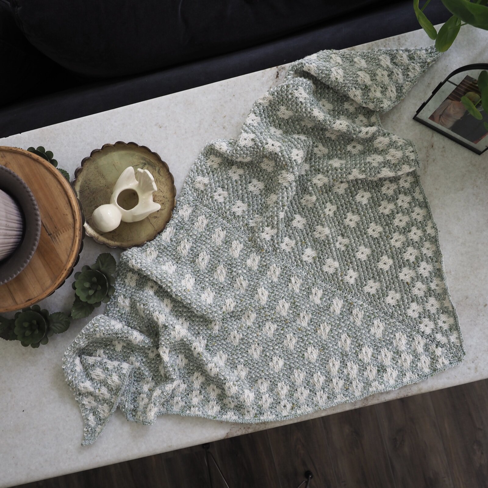 Top view of a light blue and white hand knit shawl with flowers in the pattern of it.