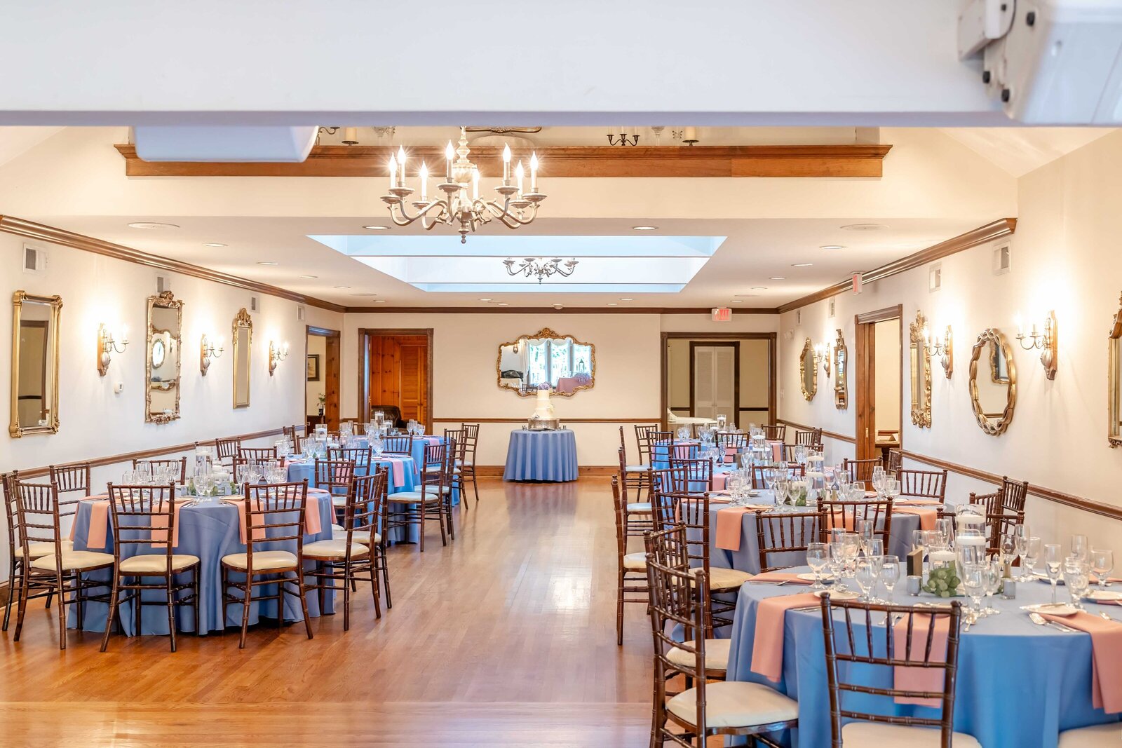 A wedding reception hall with round tables decorated in blue and peach accents, featuring chandeliers, mirrors, and elegant place settings, captured during a Wilmington, DE wedding, blending sophistication and charm.