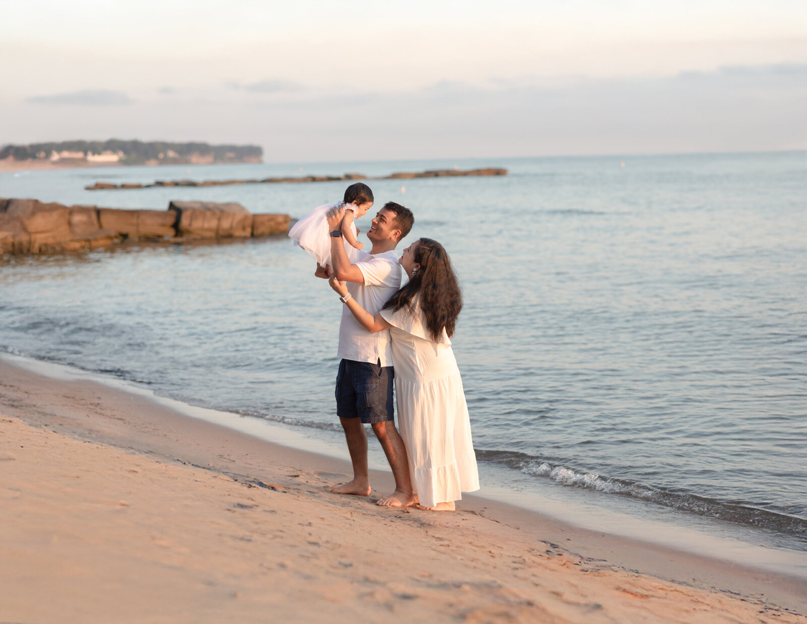 mom and dad holding daughter up in air for beach family photo session