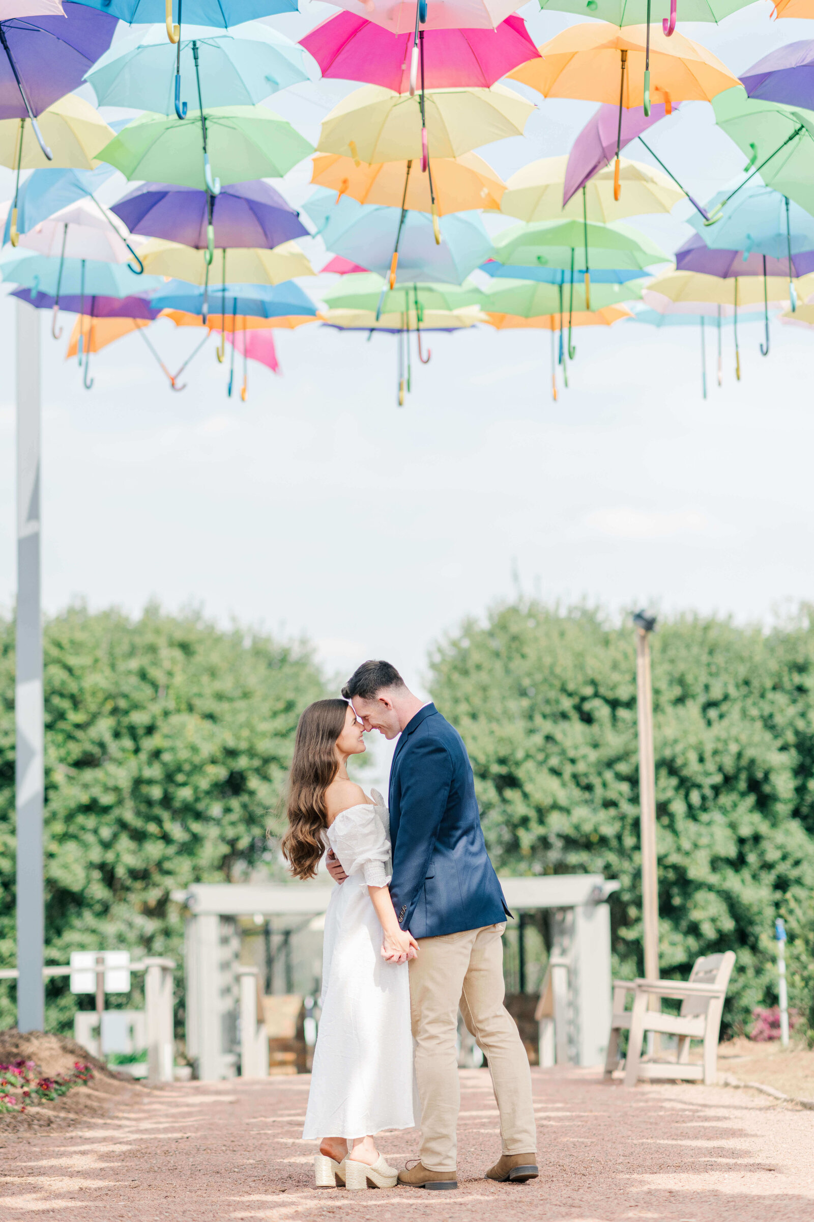 Engaged couple posing with heads touching under colorful umbrellas while holding hands for engagement photos