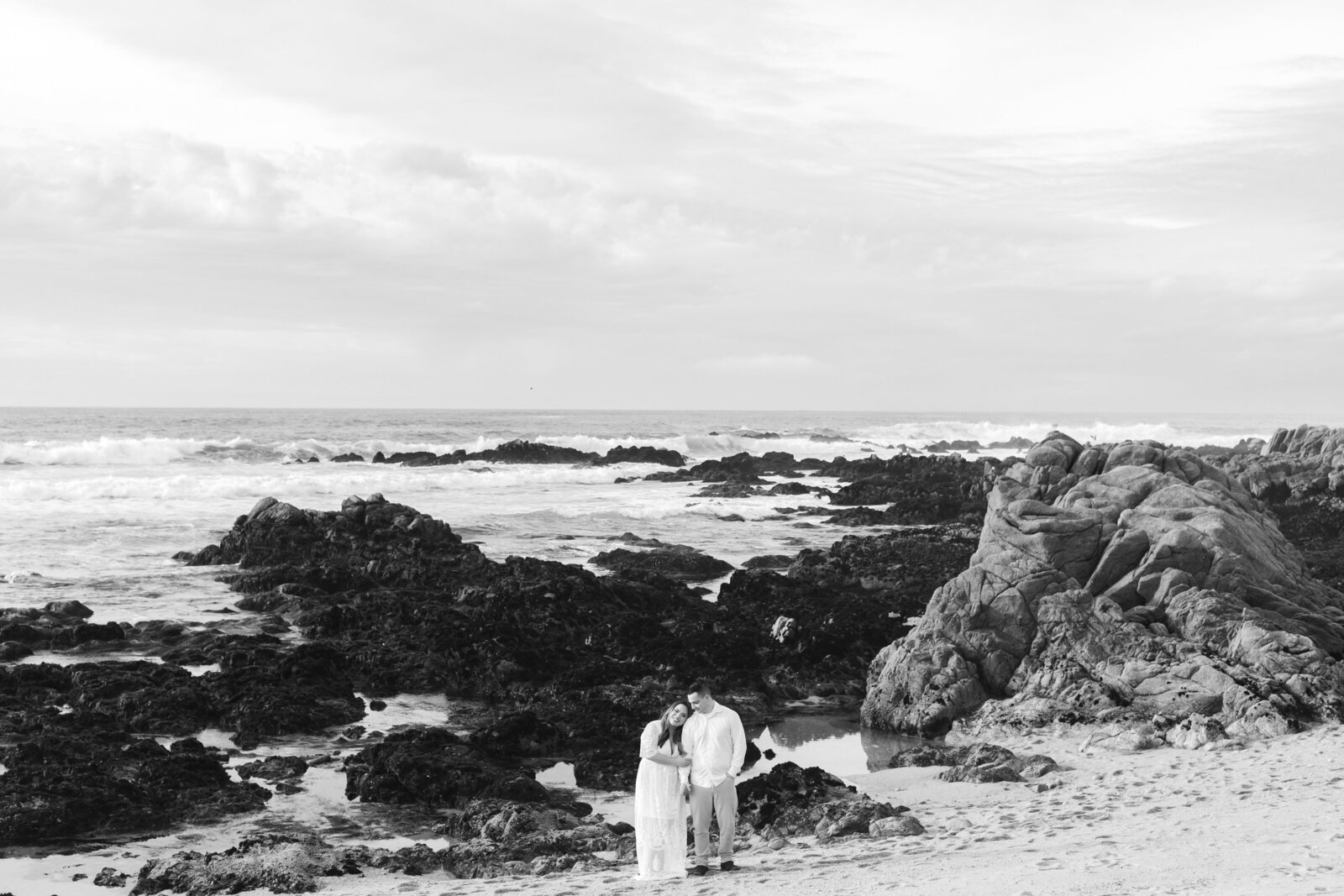 An engaged man and woman take photos on the beach in Pacific Grove, Monterey, California near Big Sur.