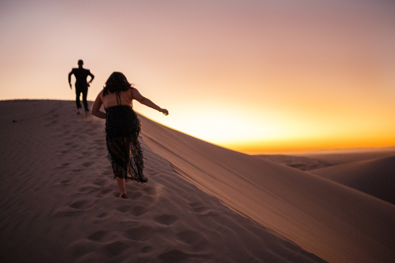 bride and groom running up ridge of imperial sand dunes