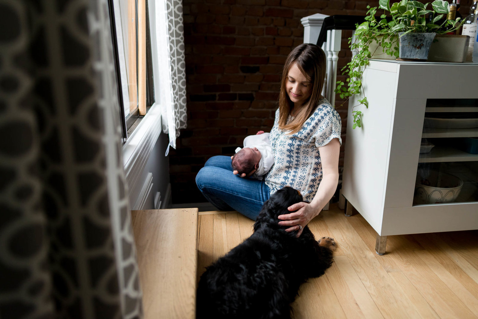 Mom caressing dog with newborn in arms at home lifestyle session