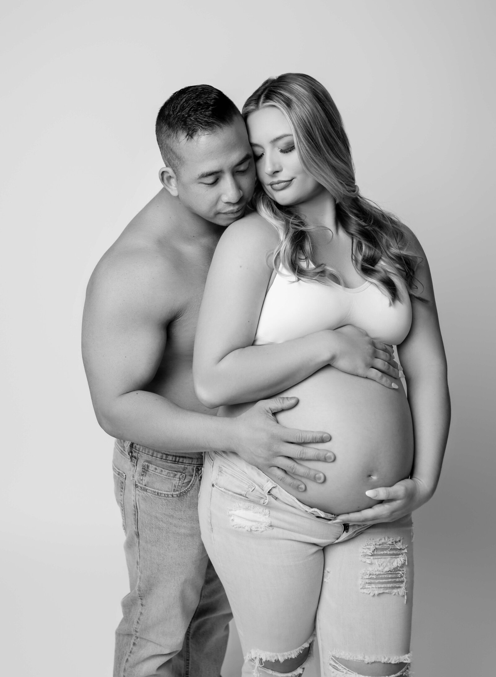 Maternity portrait of Mo and Dad in jeans and cuddling while holding baby bump. Maternity portrait taken by Jenni. Nikki Photography at Atlanta Photo Studio. 