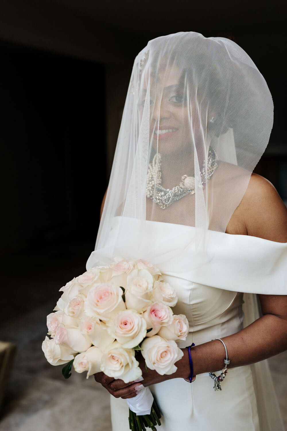 Bride smiling under a veil, holding a bouquet of pink roses