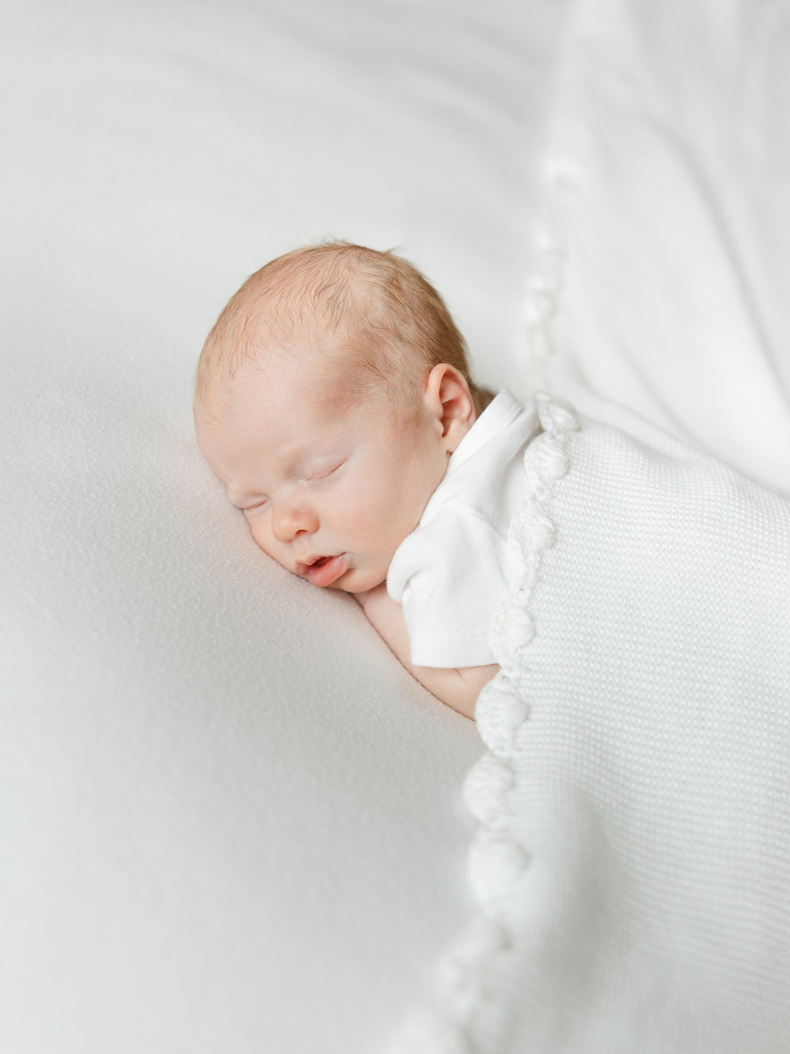 newborn sleeps on belly with textured white blanket