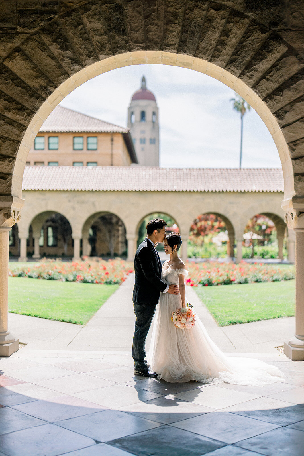 The bride and groom share a romantic kiss in the iconic courtyard of Stanford University, capturing a timeless moment.