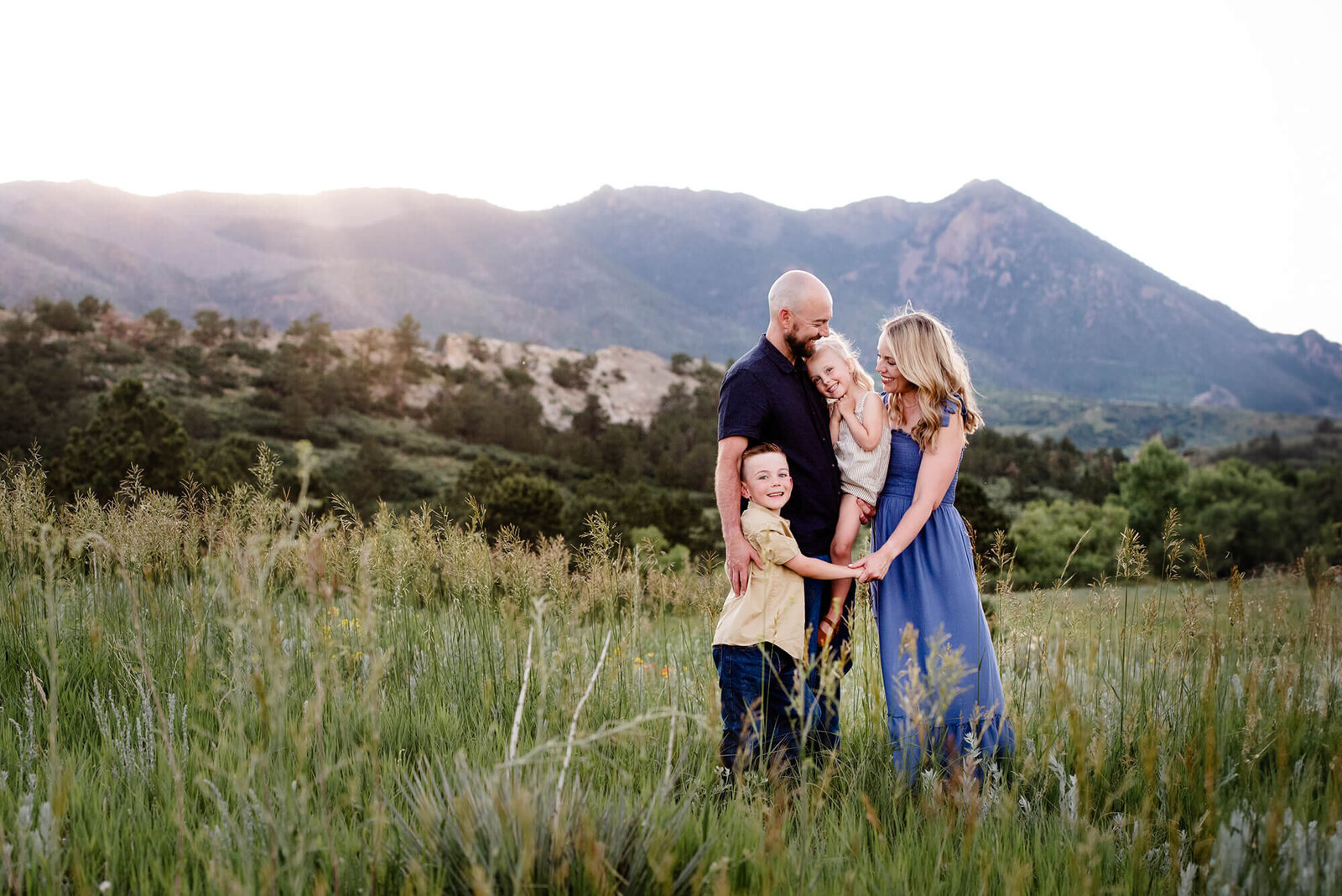 A mom and dad hug their toddler son and daughter while standing in a field at sunset for a Denver family photographer
