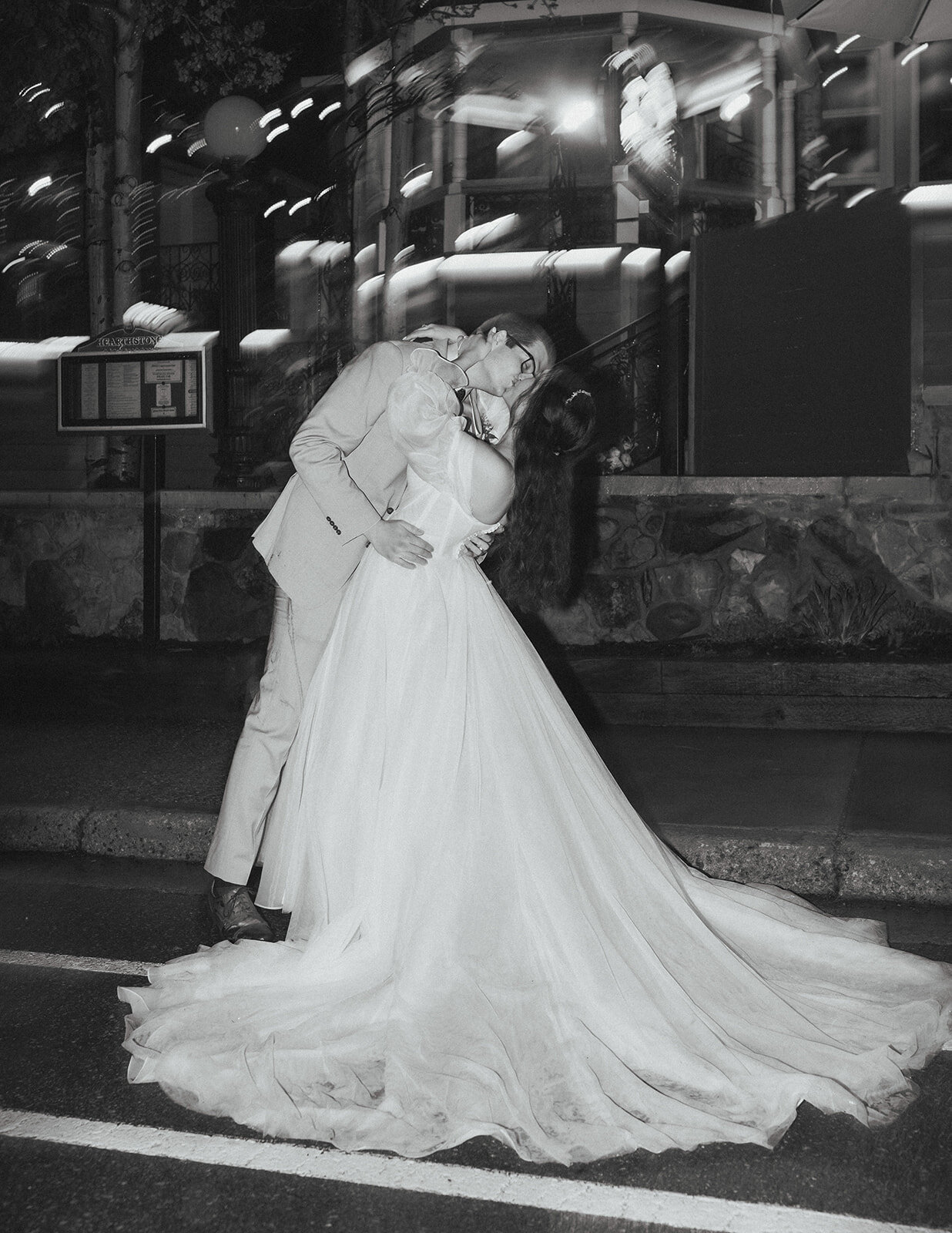 Black and white photo of bride and groom kissing each other on the street
