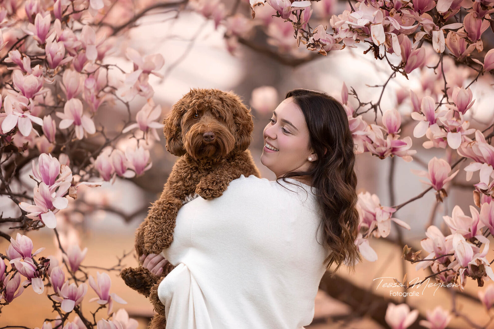 Baasje in een knuffel met haar hond bij een magnolia