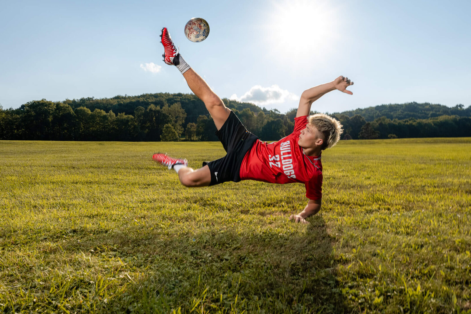 portrait of a senior kicking a soccer ball in the air in a field