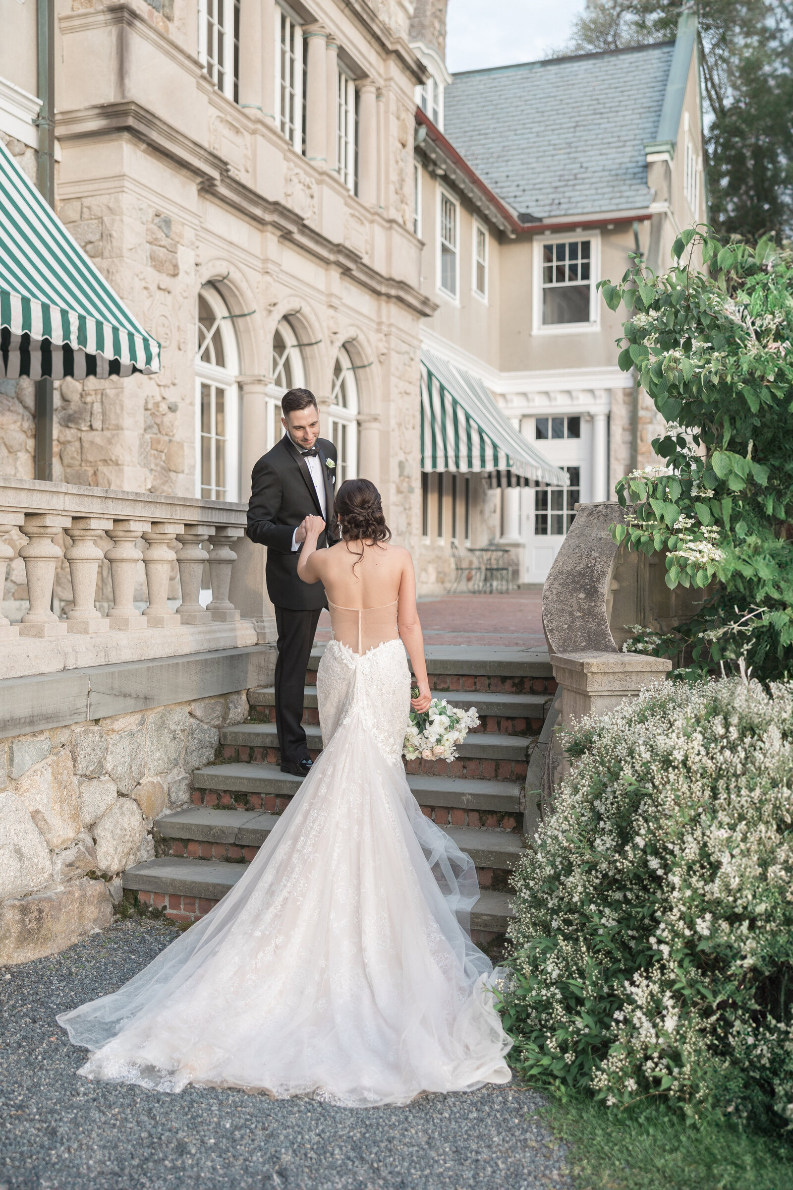 A groom leads his bride up the stairs of Blithewold Mansion