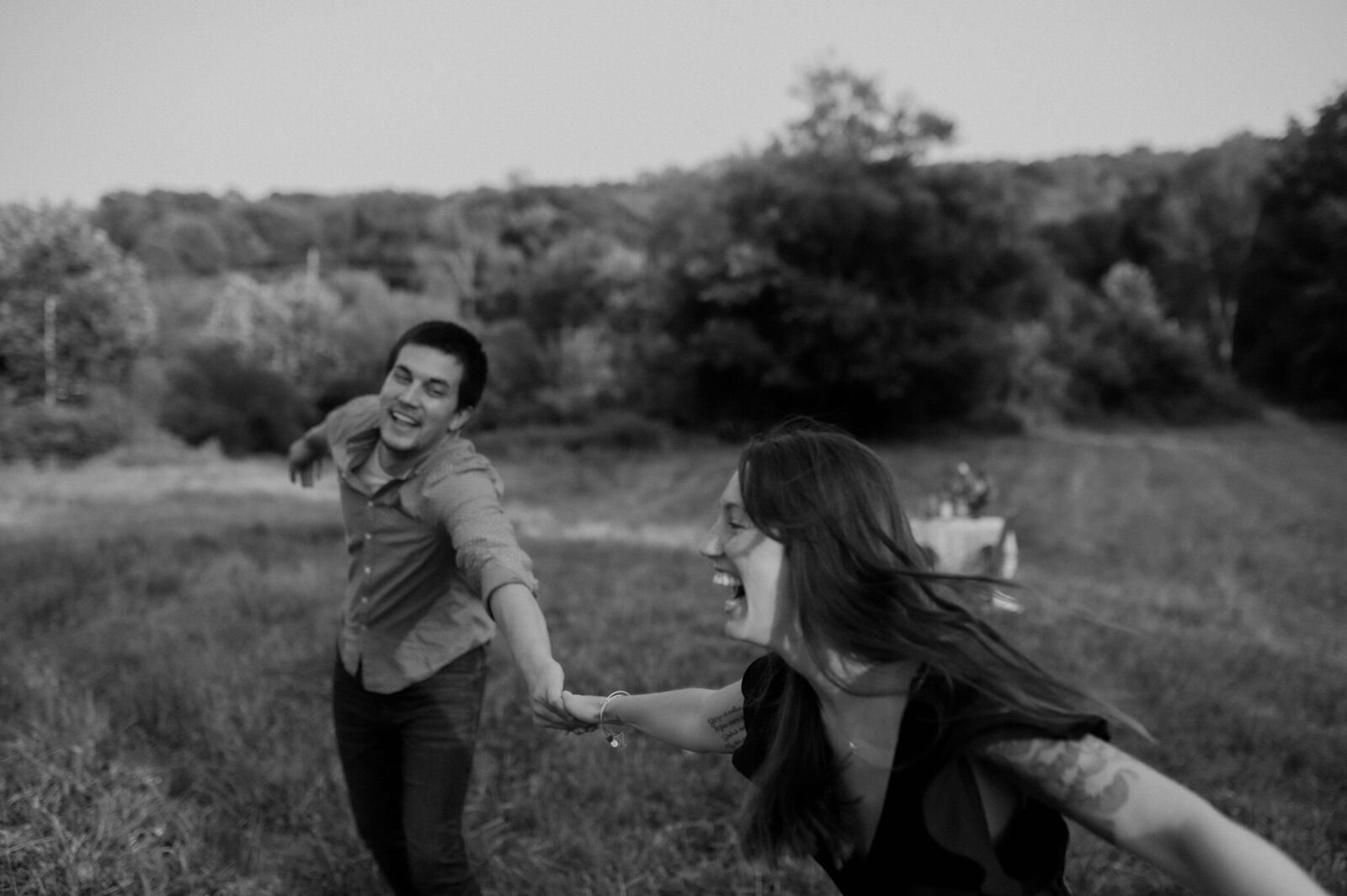 couple holding hands playfully running through field laughing and twirling