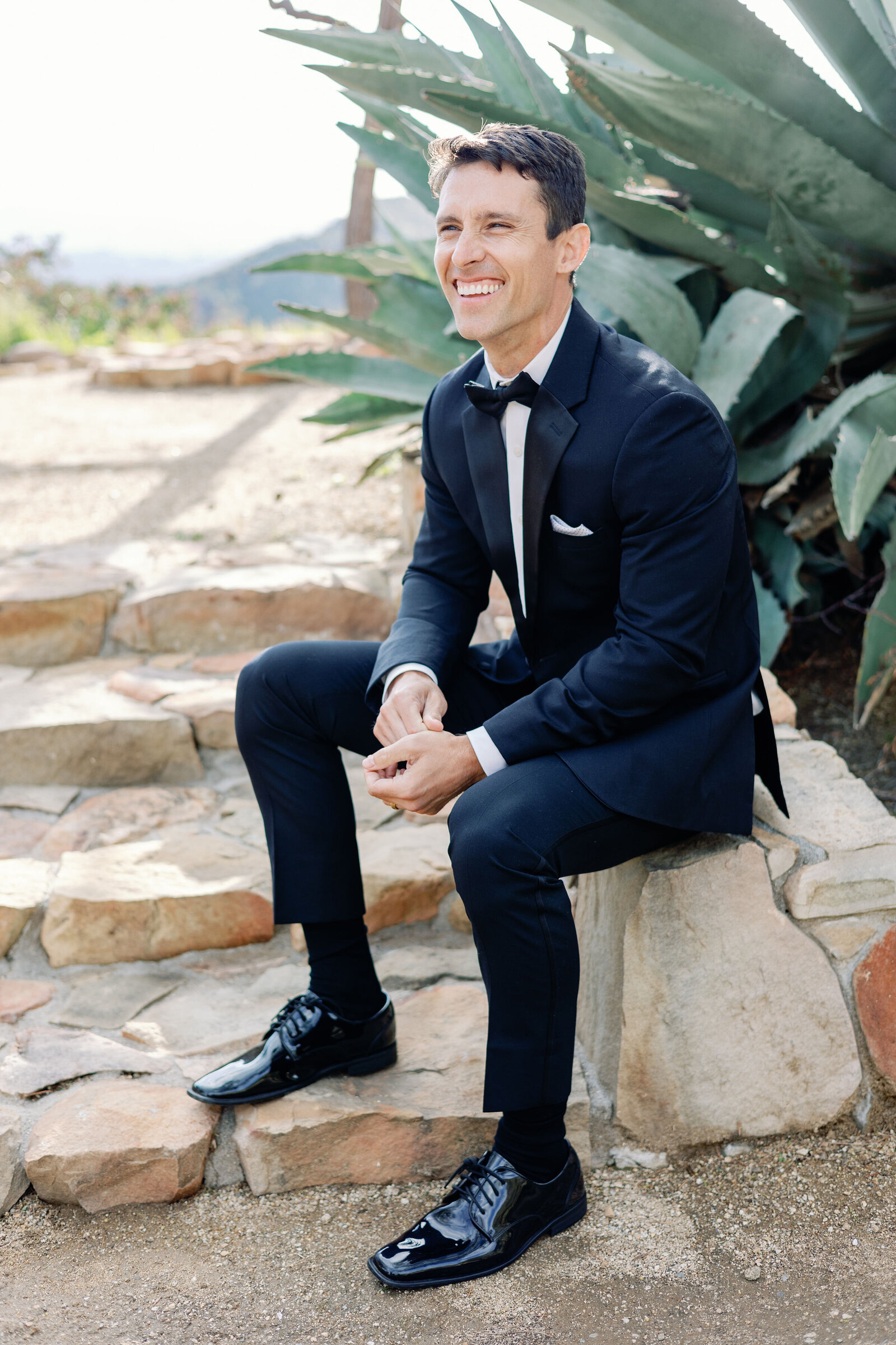 wedding portrait of groom sitting on a stone stair path and smiling captured by wedding photographer bay area