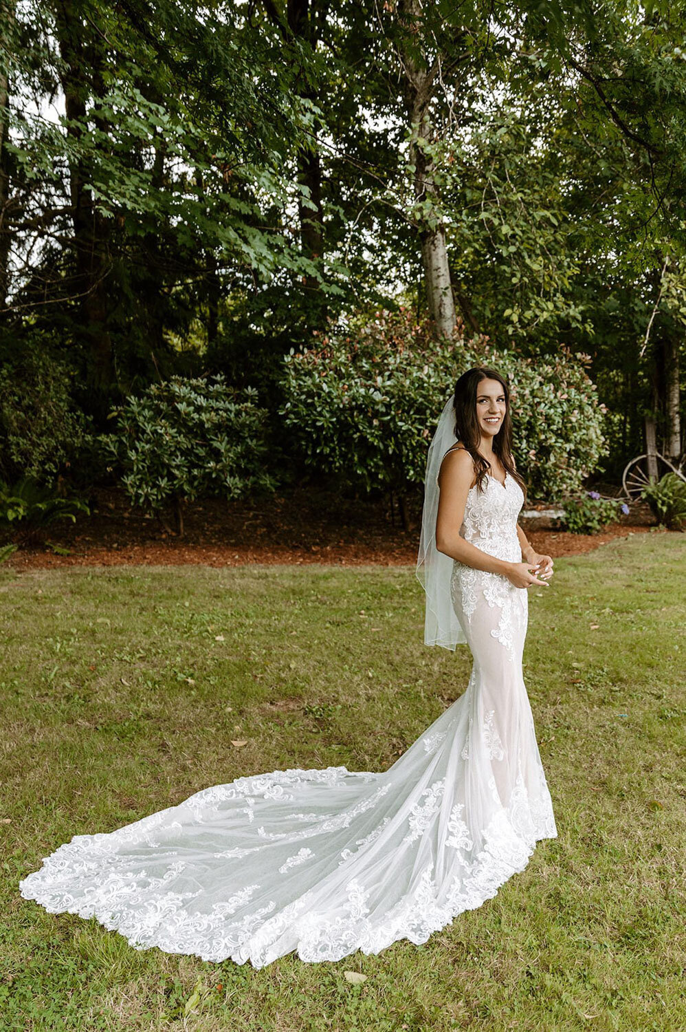 A bride posing in a fitted lace gown, surrounded by greenery