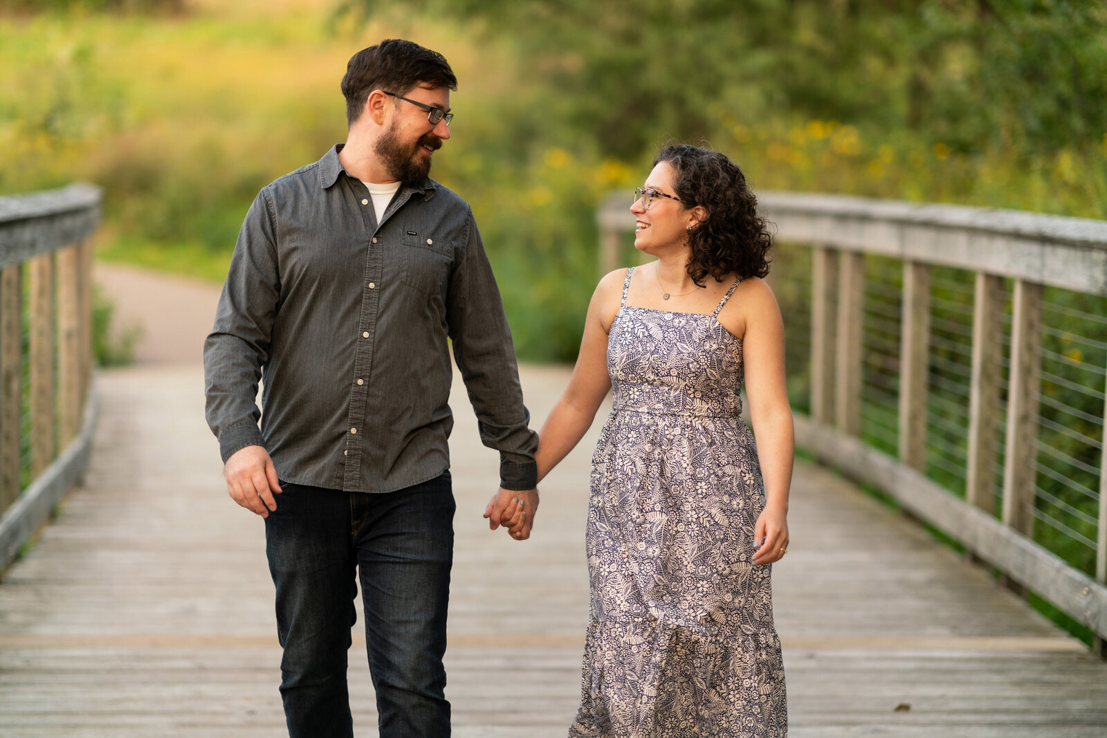 Man and woman cross bridge smiling at sunset.