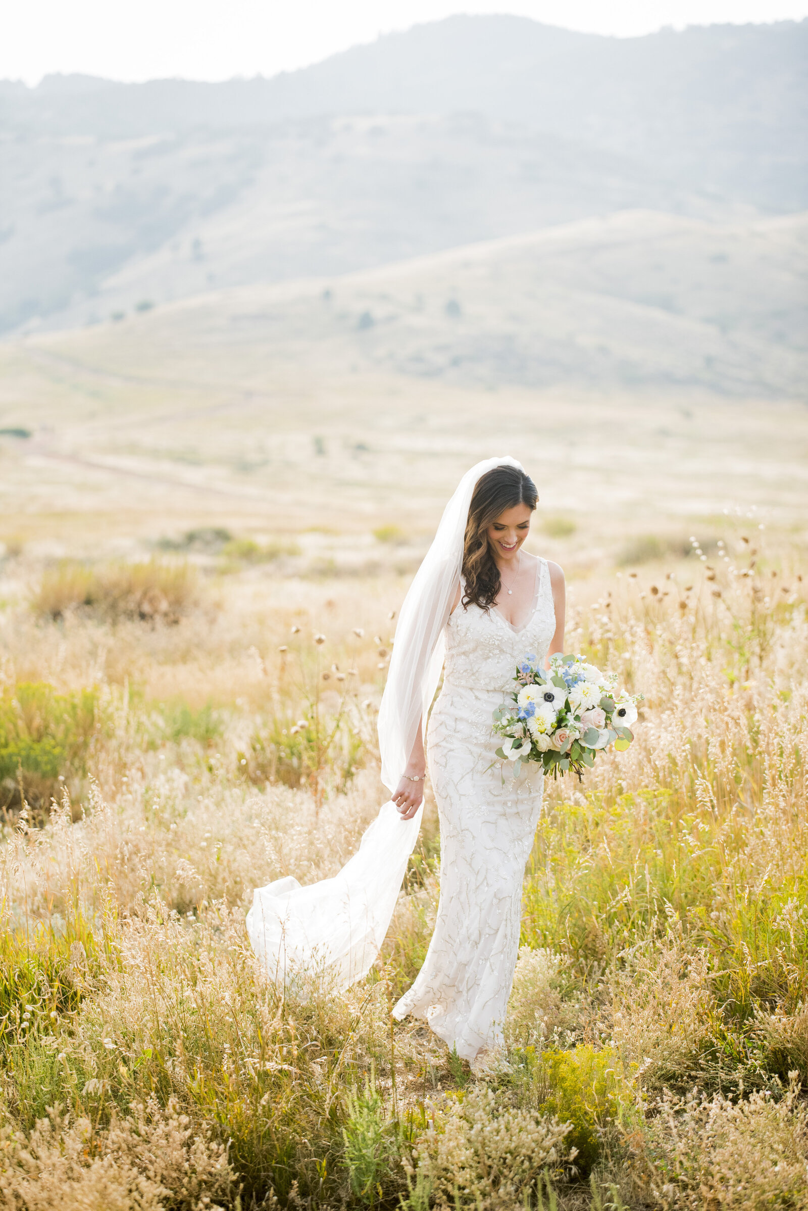 A bride walks through a field carrying her bouquet at The Manor House in Littleton, Colorado.