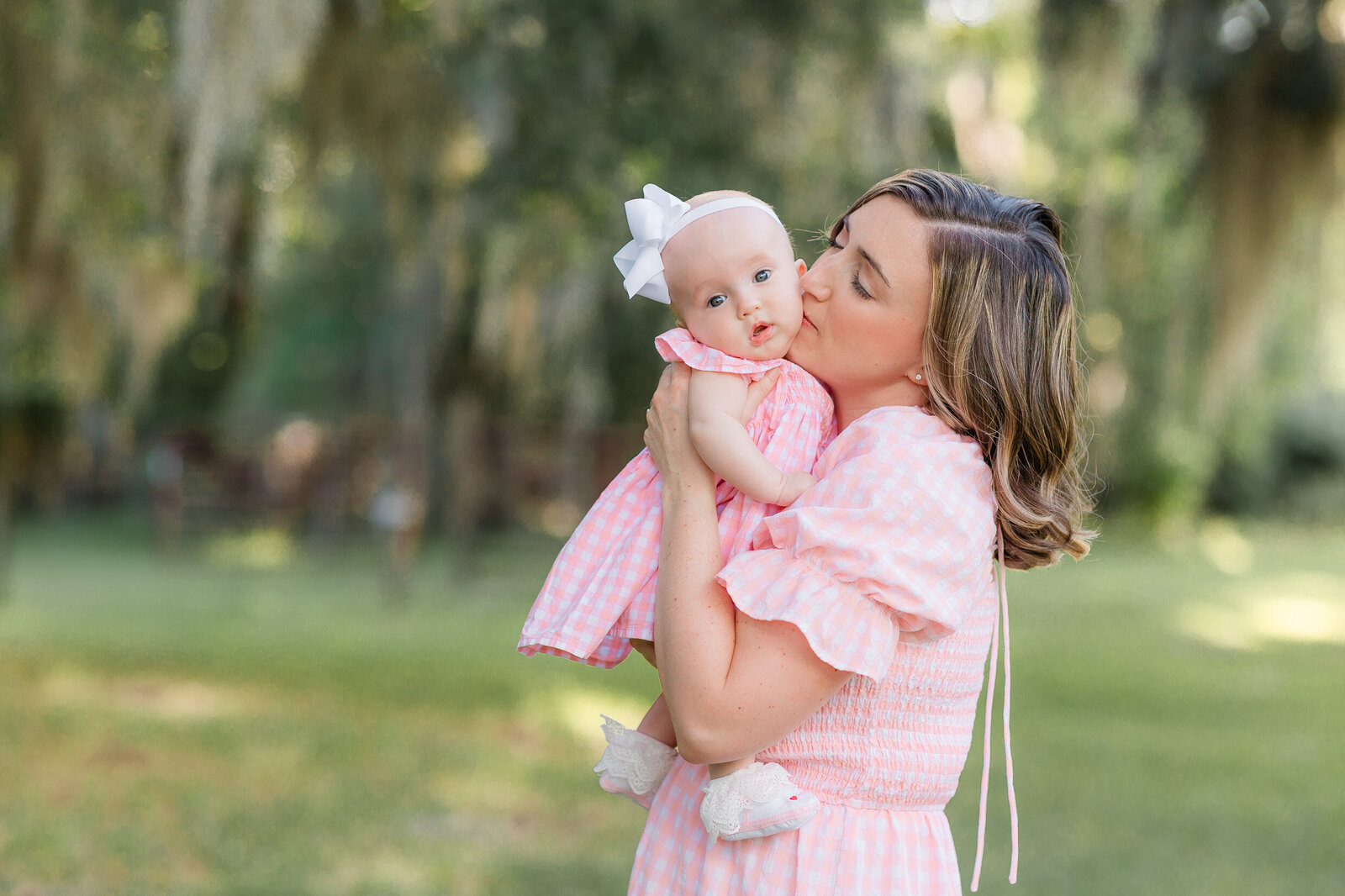 Mom in her 30;s holding her 4 month old wearing matching pink dresses looking at the camera and smiling