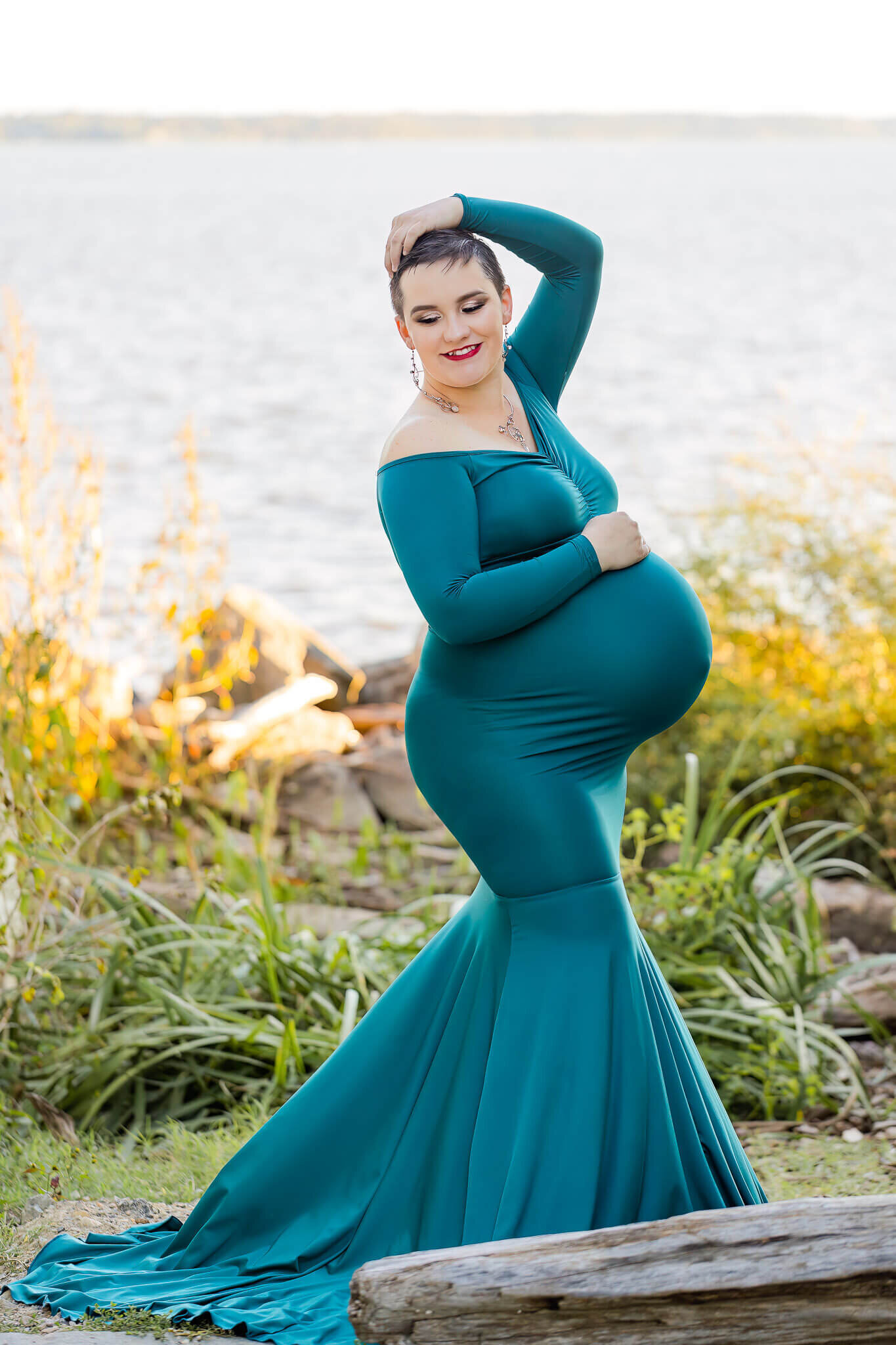 A beautiful pregnant woman posing in front of the water at an Alexandria park at sunset.