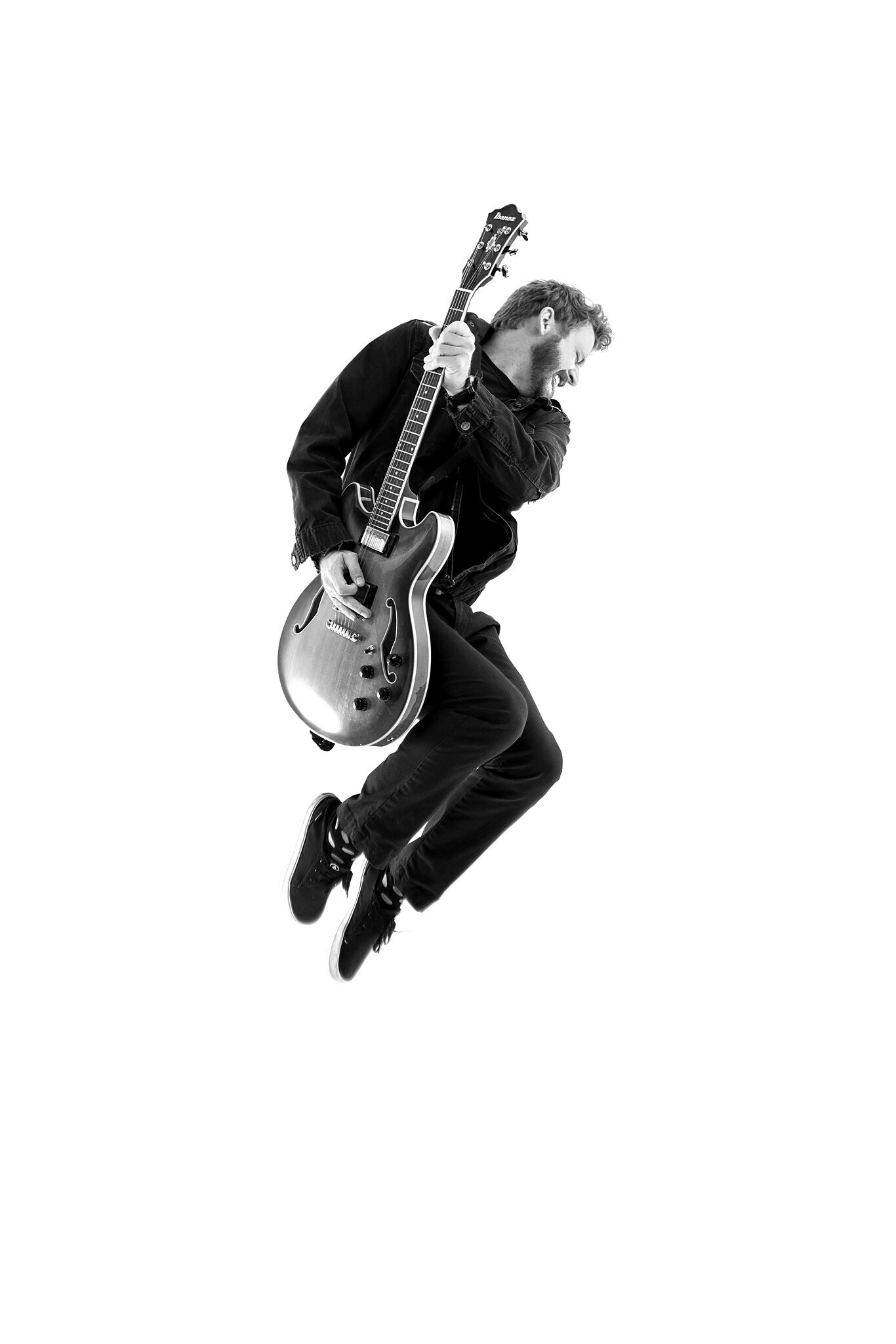 A man wearing dark clothing jumps in the air while playing an electric guitar, set against a plain white background—perfect for music photography Jacksonville.