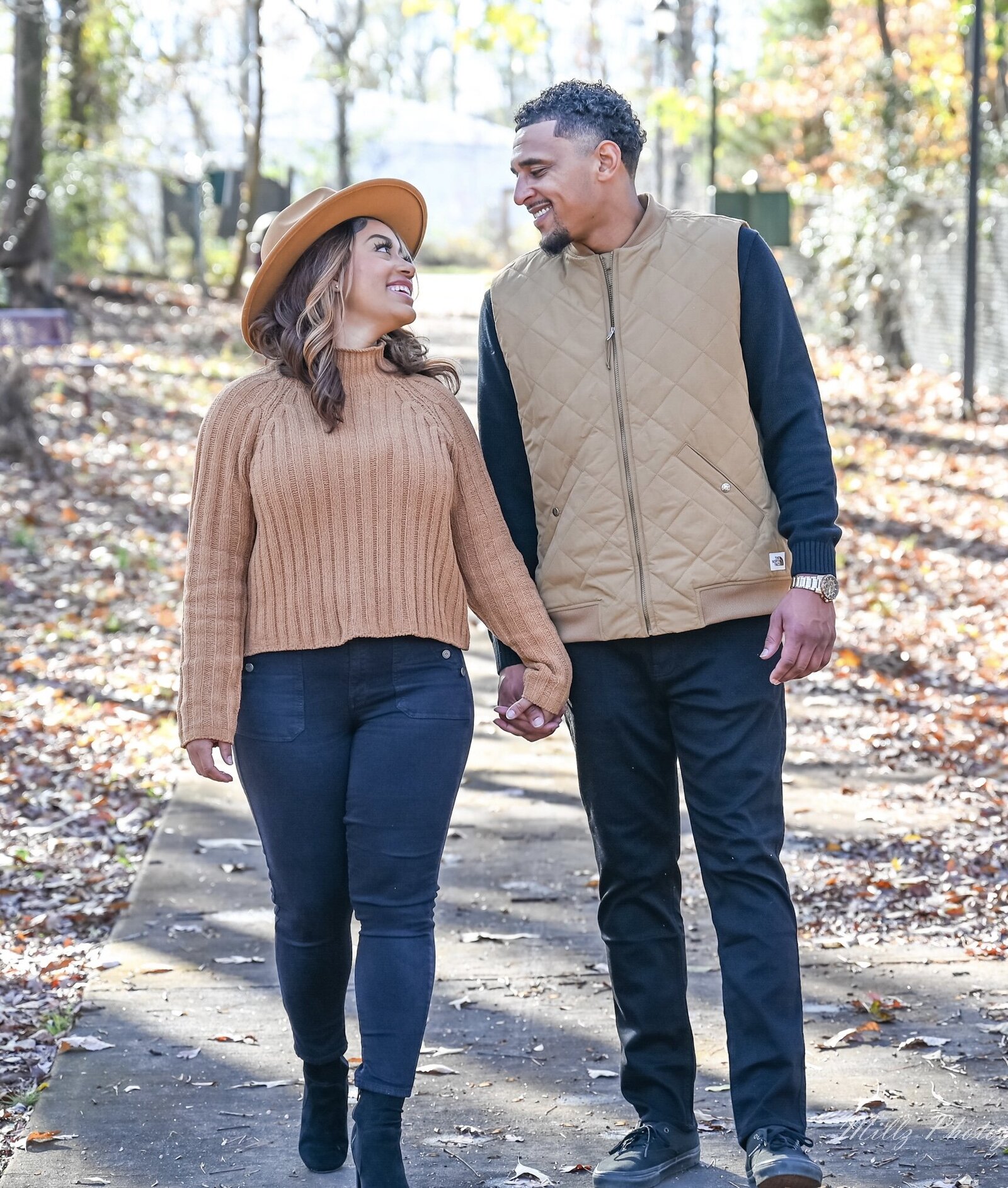 woman in a hat holding hands with a man walking through the woods in the fall photographed by Millz Photography in Greenville, SC
