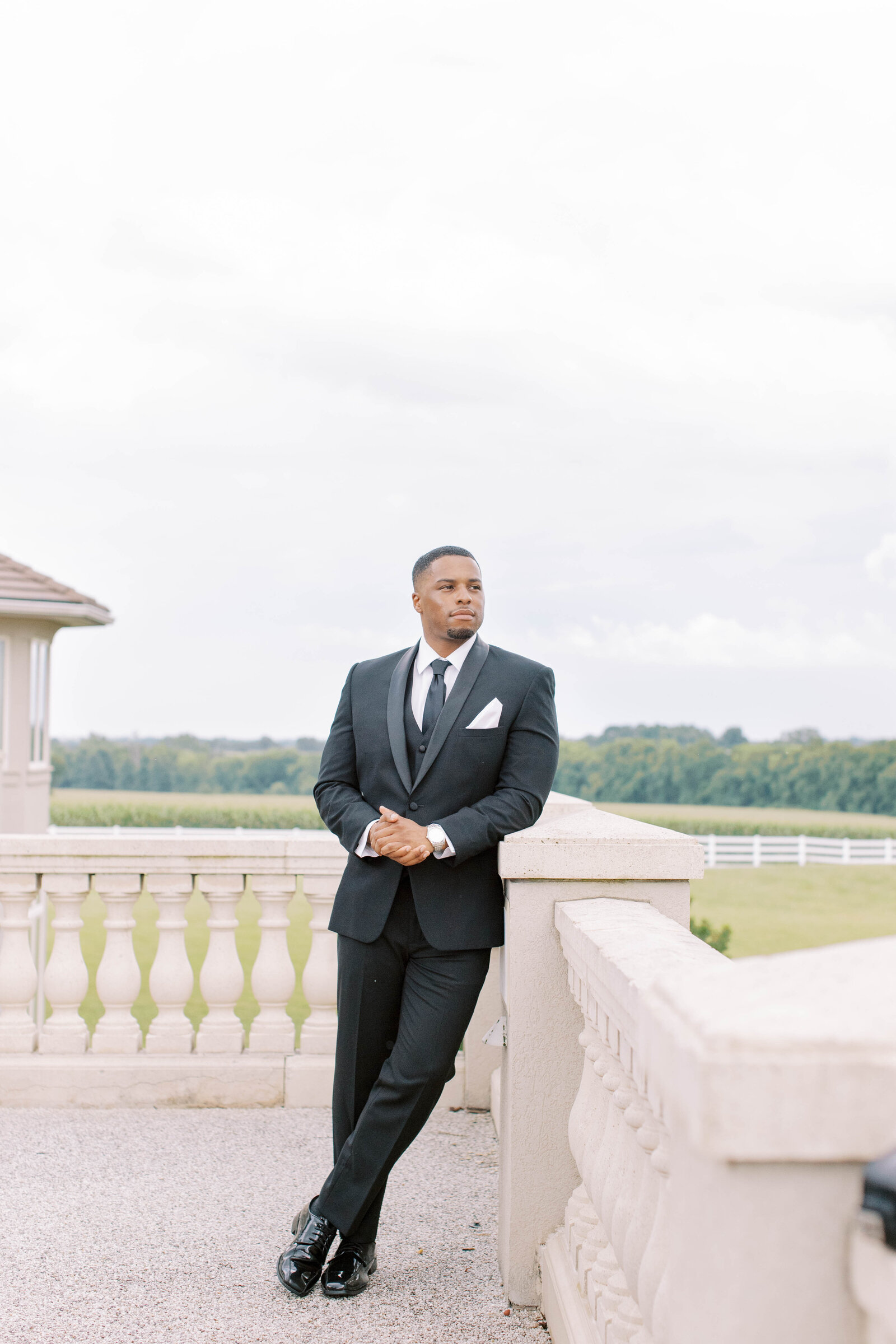 Grooms stands at wedding venue Bourgmont Winery overlooking the scenery in Kansas