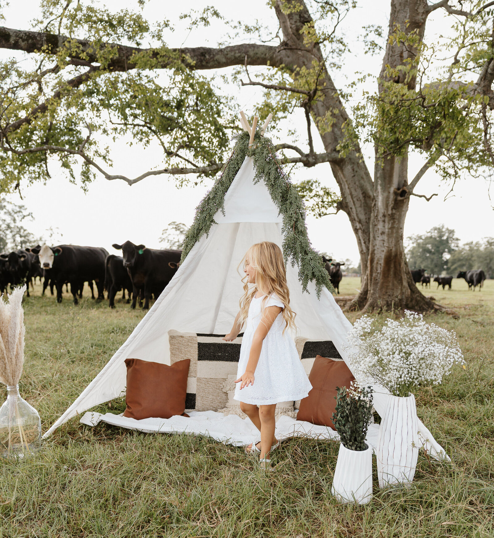 Little girl standing by a boho white teepee setup during a children's session in a farm field in Aiken SC.