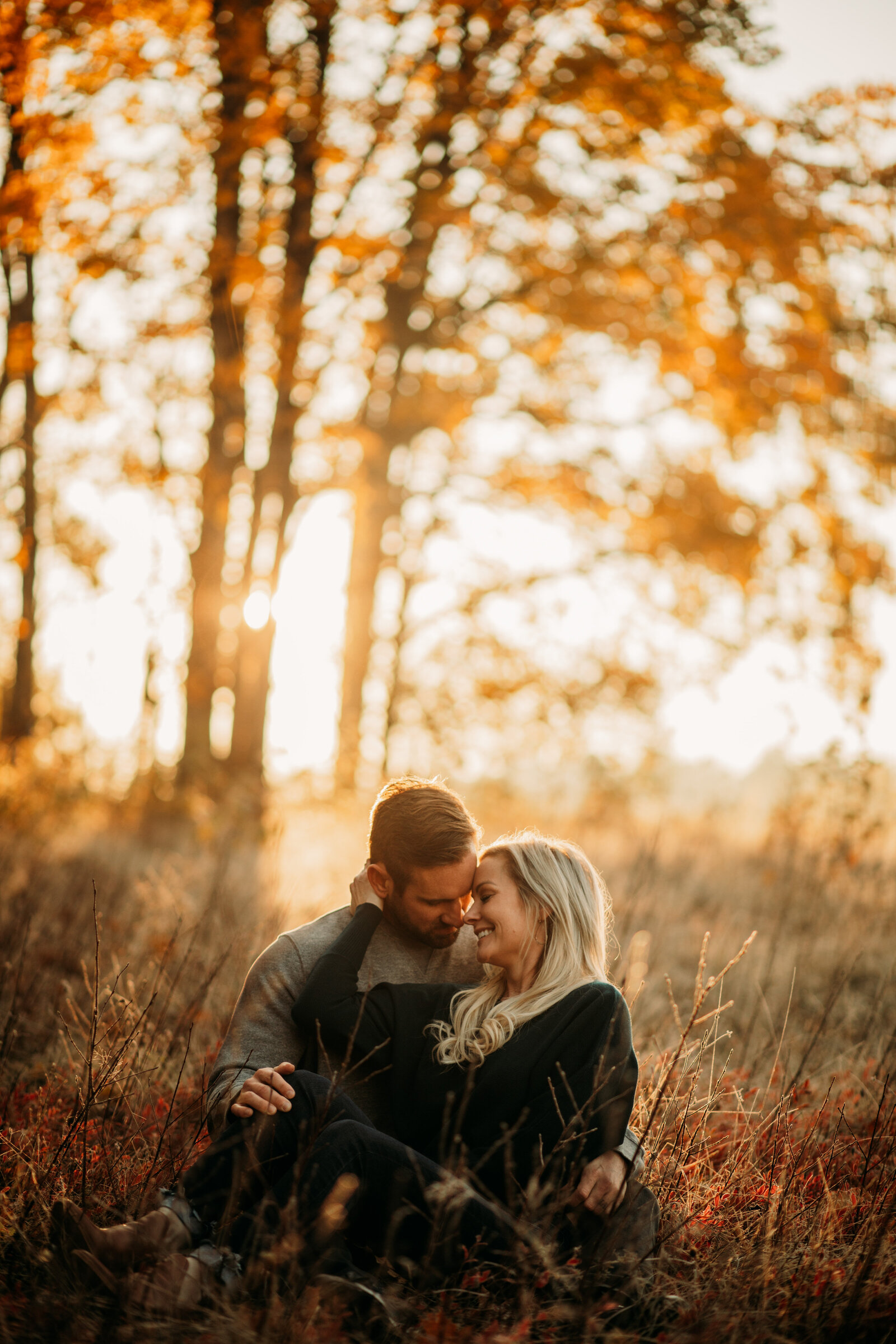 boyfriend and girlfriend sit in a field during sunrise in maine during foliage fall