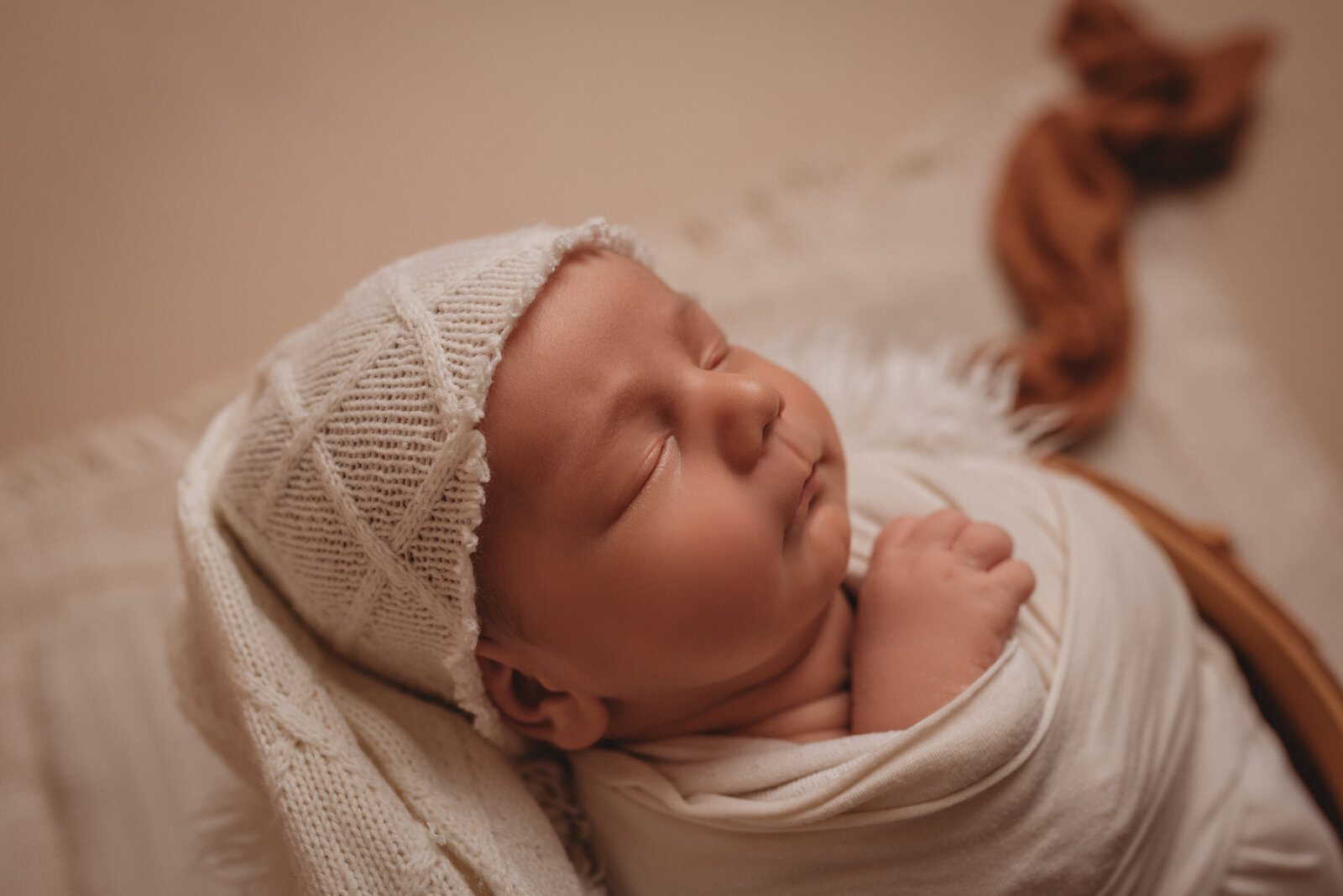 Newborn boy at his newborn portrait session wearing a white hat and white swaddle