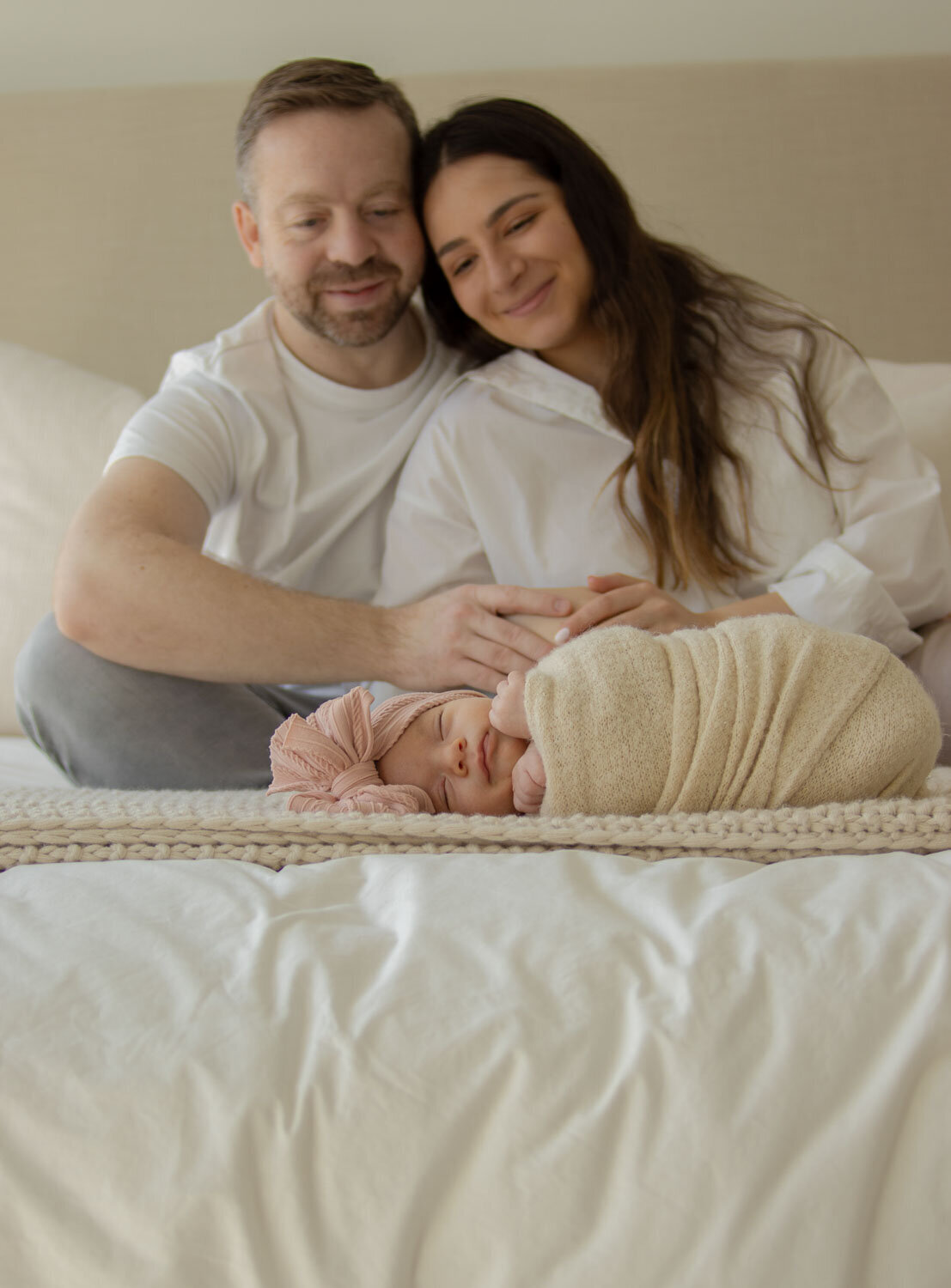 Family sitting on a bed with their newborn baby wrapped in a blanket