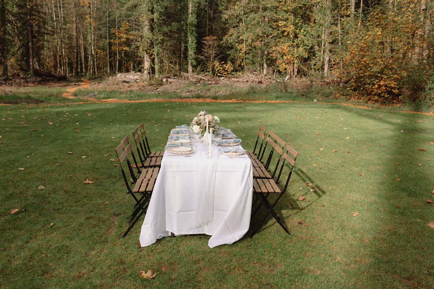 Outdoor dining table set in an open grassy field with wooden chairs