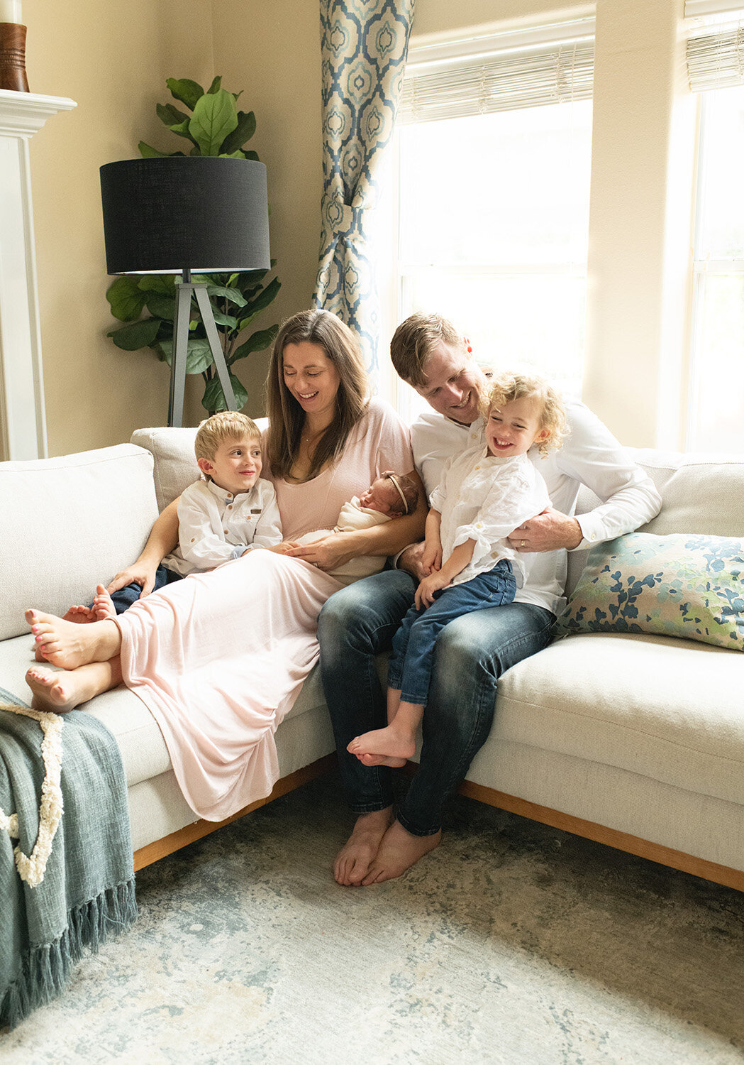 Parents and siblings cuddle on the couch with their newborn in a warm, relaxed setting. A lifestyle newborn session by Moments in Light Photography.