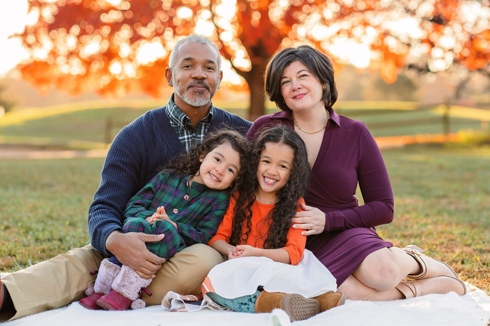 A family of four sitting on a blanket in front of fall foliage
