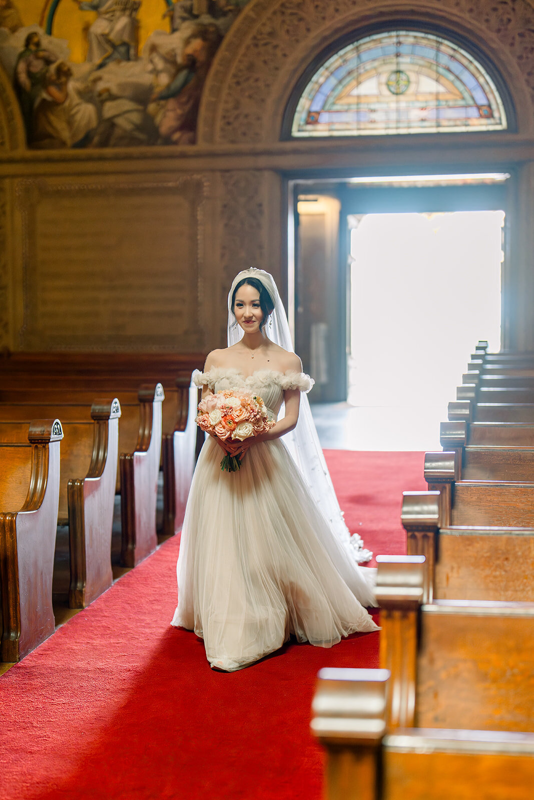 The bride stands gracefully holding her bouquet at the aisle of Stanford Memorial Church, capturing a moment of pure elegance.