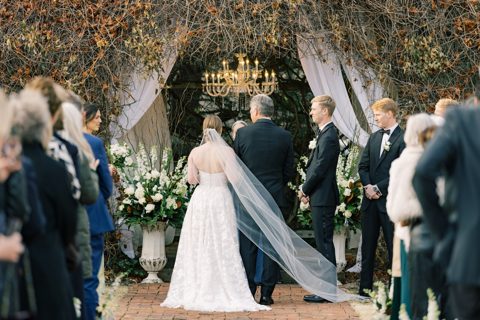 Bride walks down the aisle with her father, holding onto his arm as he lovingly gives her away, capturing a heartfelt wedding ceremony moment.