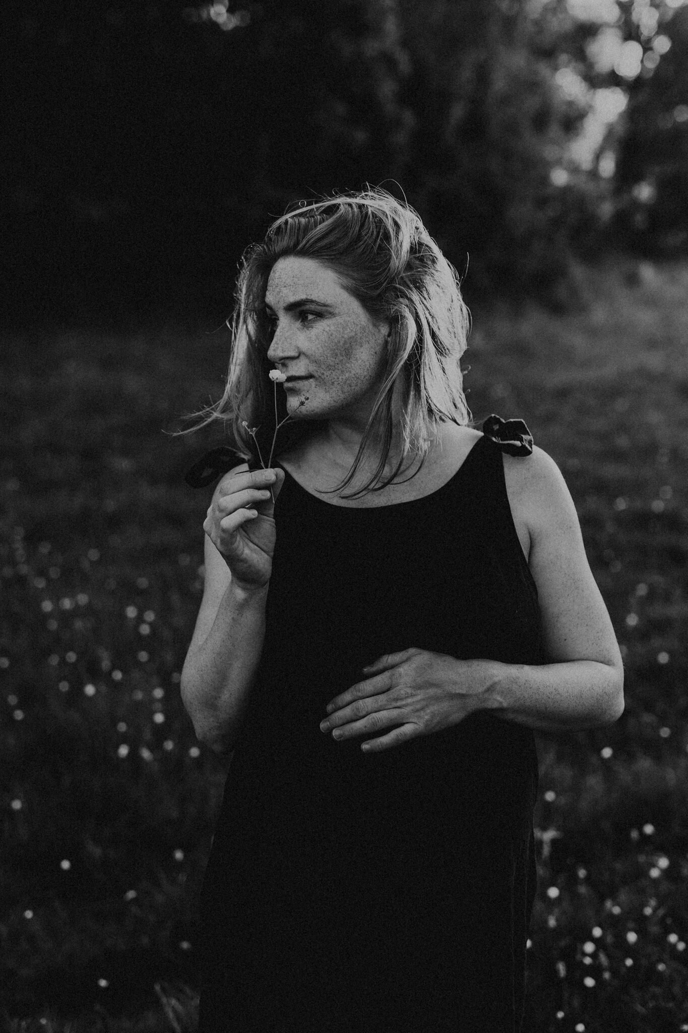 en gravid mamma i linneklänning luktar på en blomma