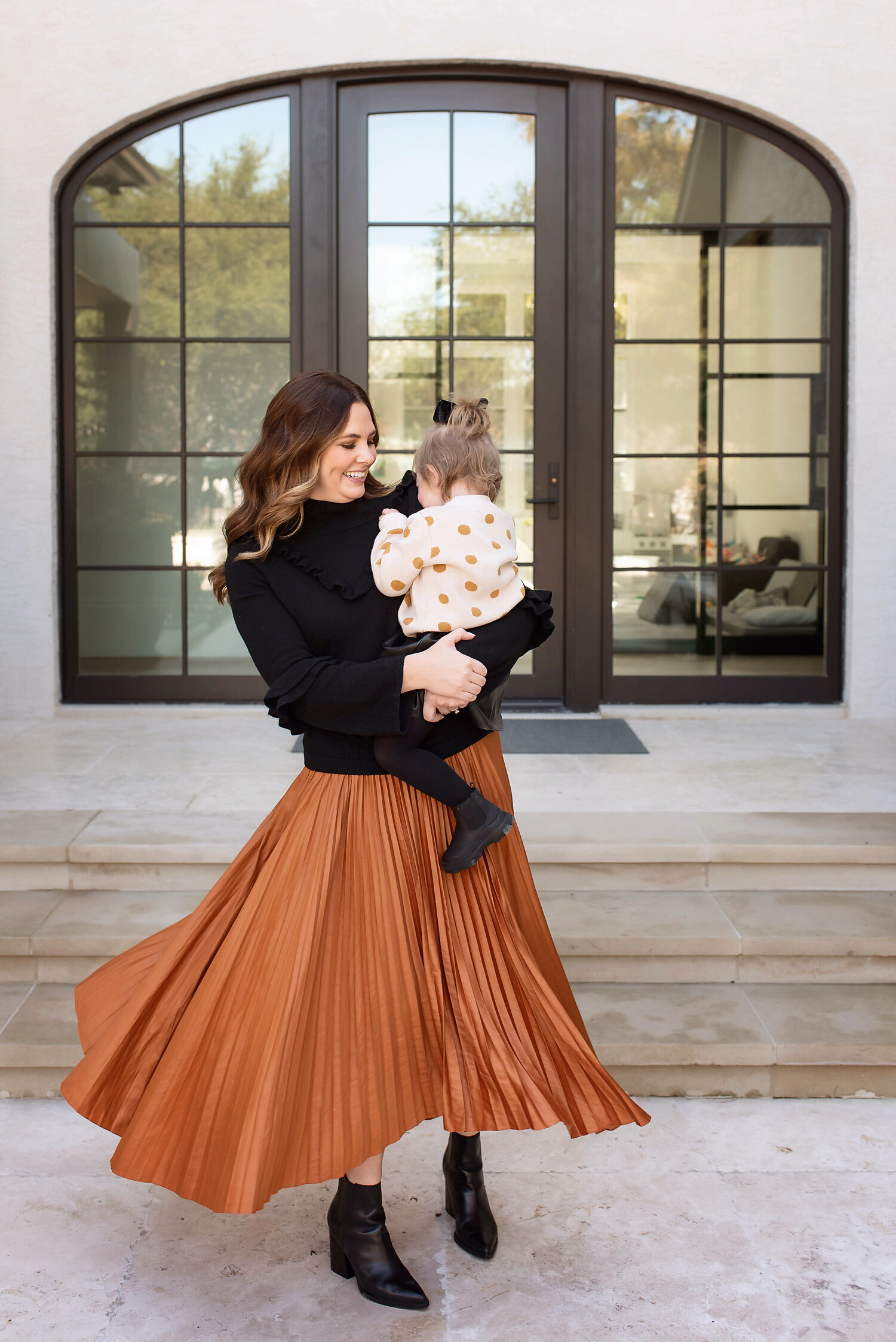 Beautiful mother wearing a rust flowy skirt twiriling around while holding her toddler daughter.